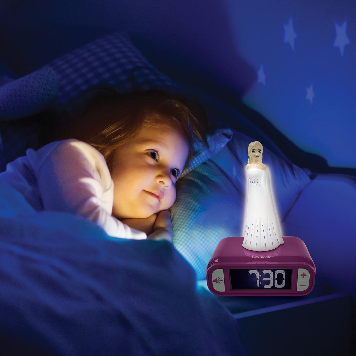 Una niña sonríe al reloj con Elsa. El reloj está en una mesa con una cama al fondo.