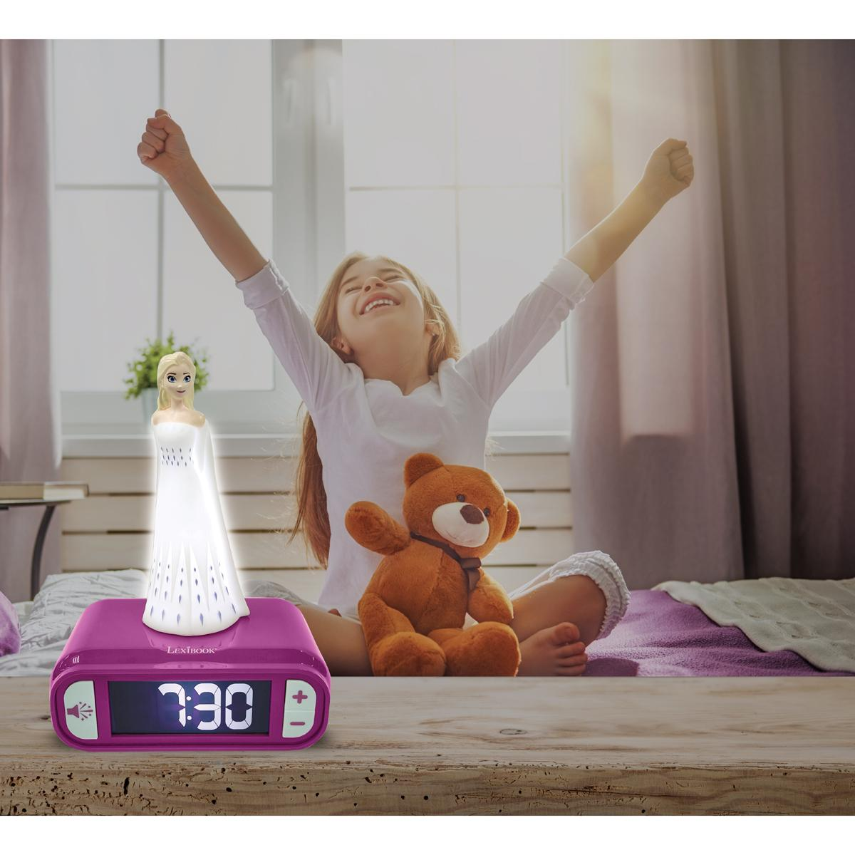 Una niña sentada en una cama con los brazos en alto. Una estatua de Elsa está en un reloj, junto a un oso de peluche.