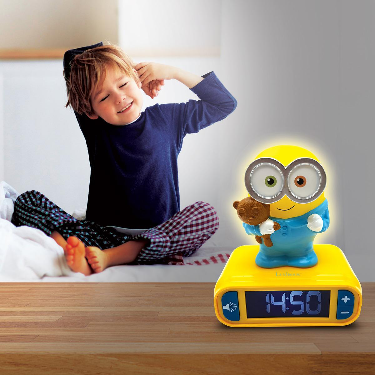 Un niño se despierta, junto a un despertador Minion amarillo con una figura de Minion encima.