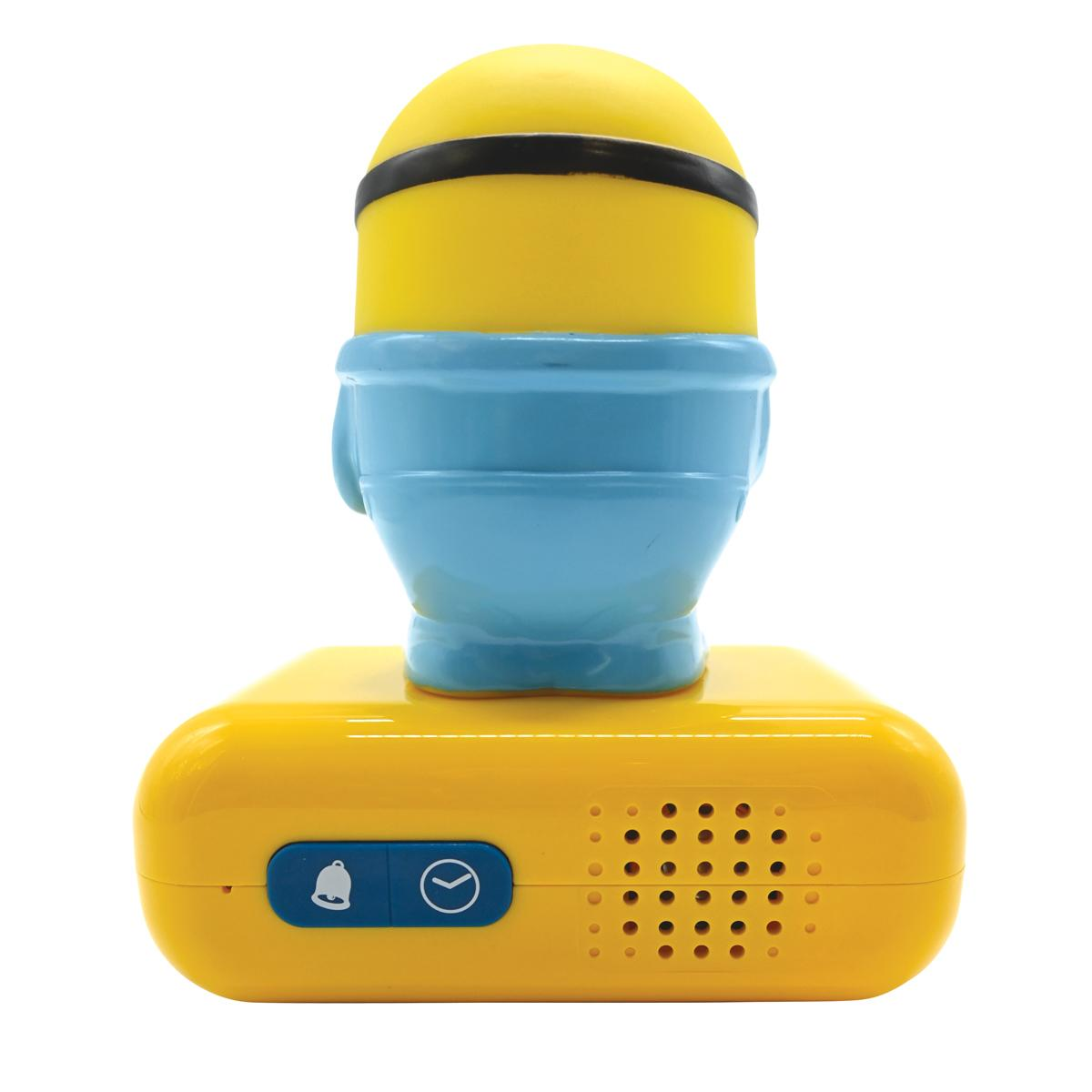 Reloj despertador amarillo en forma de Minion con detalles azules, botones y altavoz sobre fondo blanco.