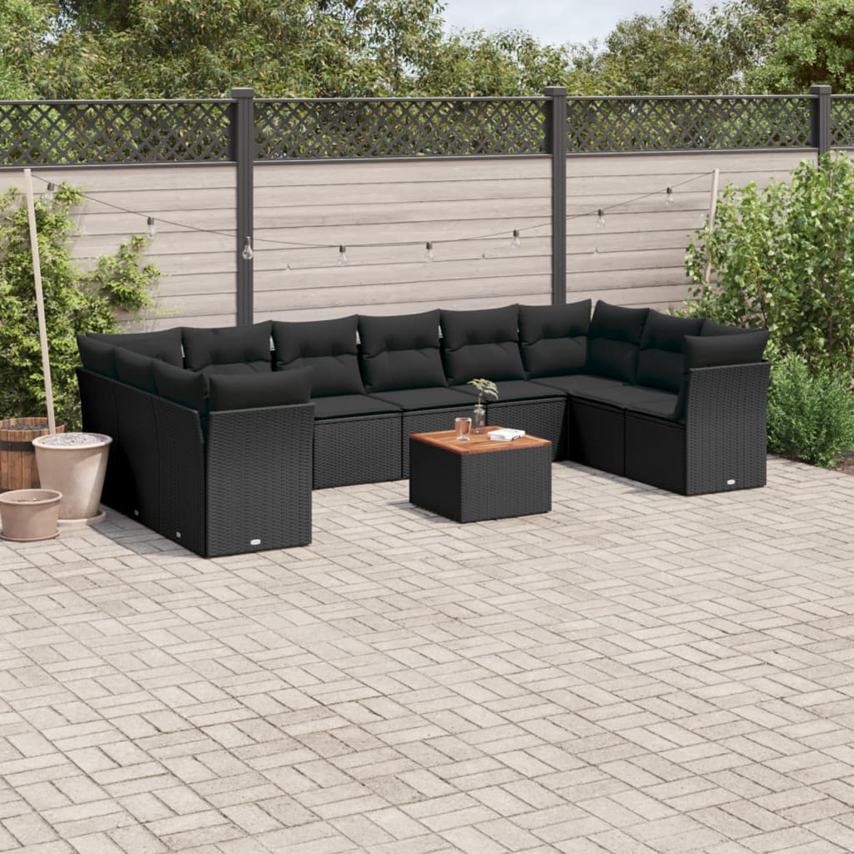 Schwarze Eck-Sitzgruppe im Freien mit quadratischem Tisch, auf einer Backstein-Terrasse, üppiger Hintergrund.