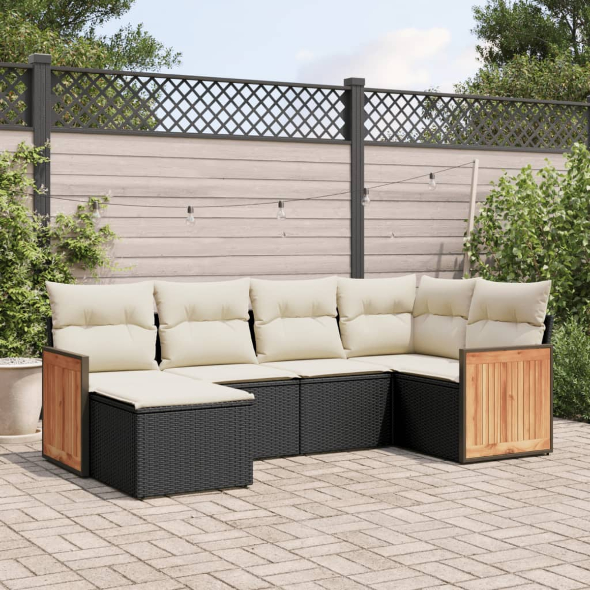 Schwarzes Rattan-Sofaset mit cremefarbenen Kissen, auf einer Ziegelterrasse.