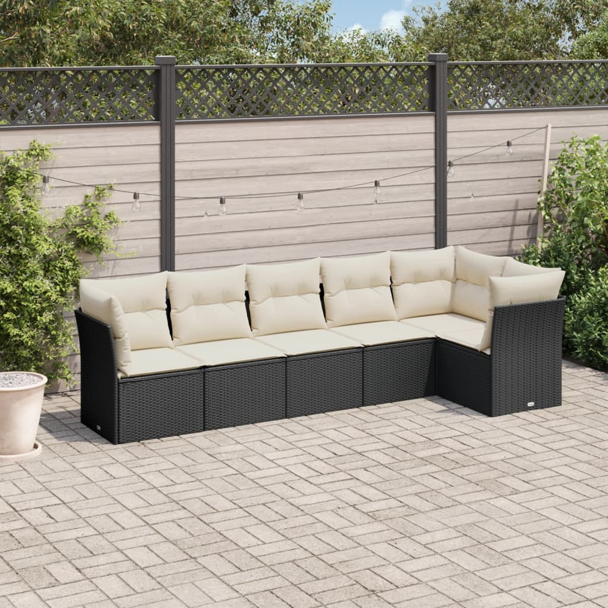Schwarzes Ecksofa aus Korbgeflecht mit cremefarbenen Kissen auf einer Terrasse.