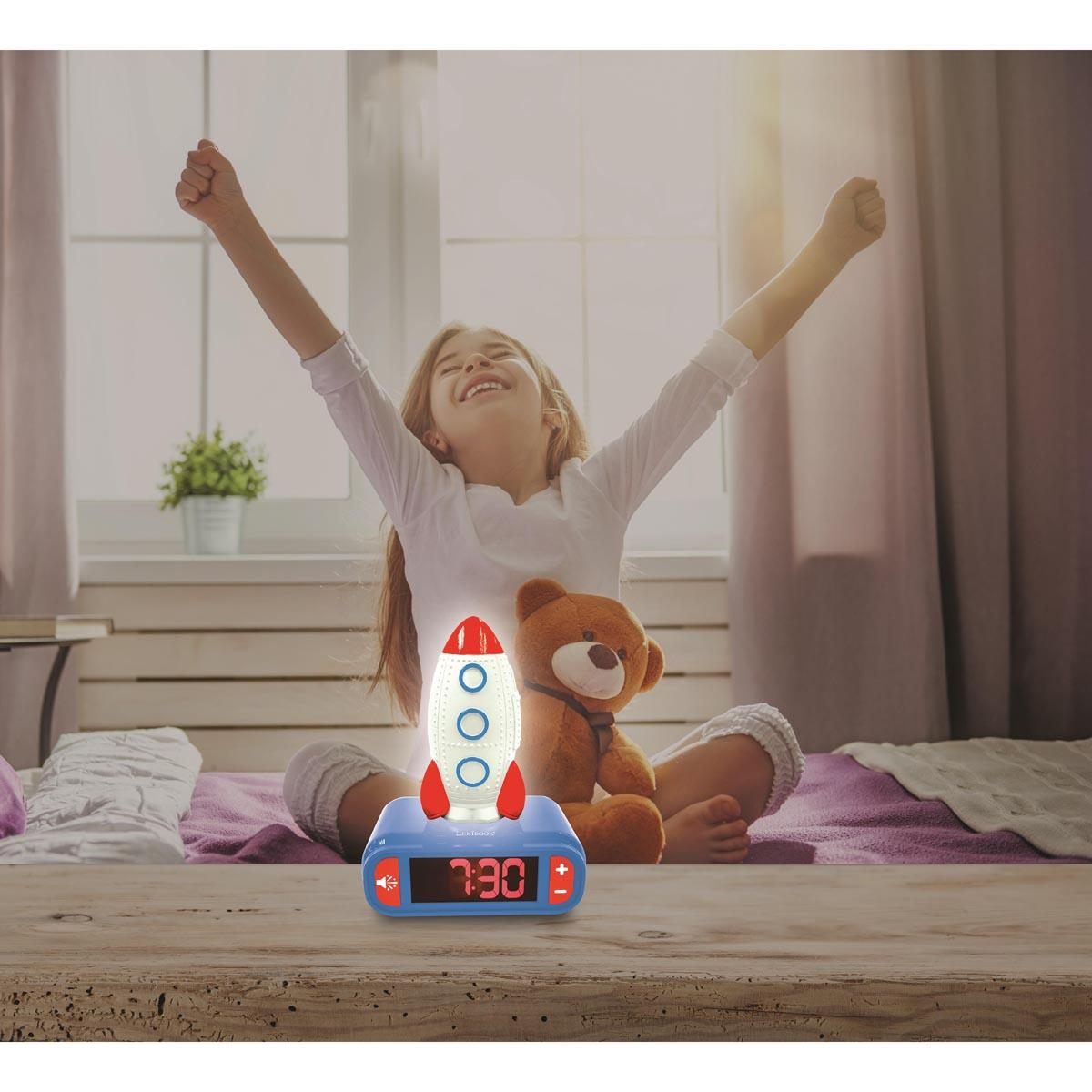 Niña con los brazos levantados, se despierta. Despertador de cohete muestra '7:30'. Oso de peluche en la cama, ventana al fondo.