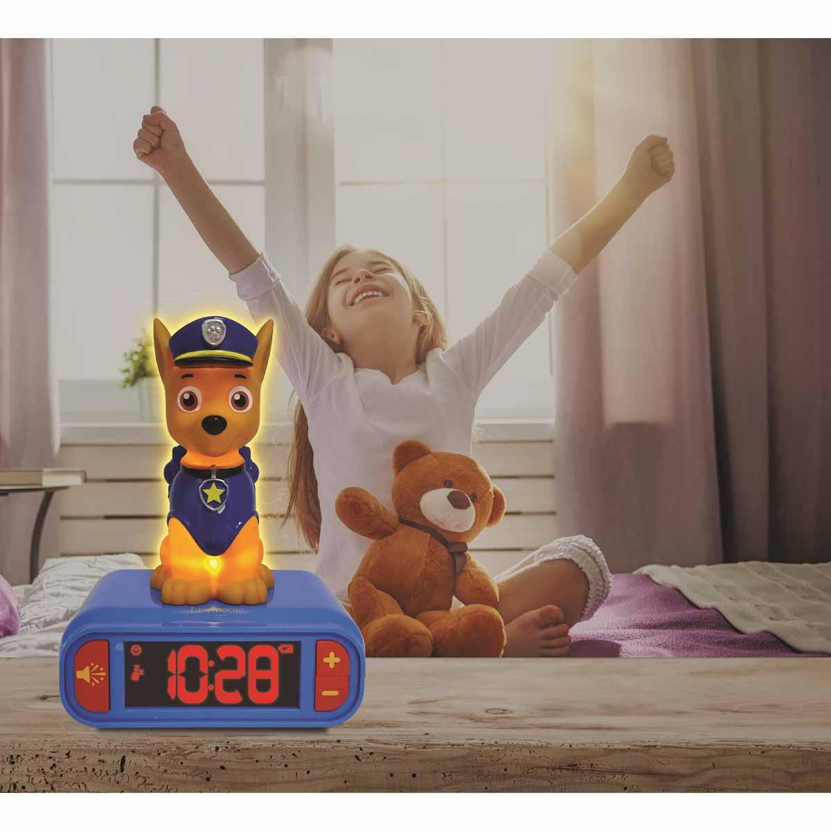 Mädchen dehnt sich neben Paw Patrol Wecker mit Chase und Teddybär.