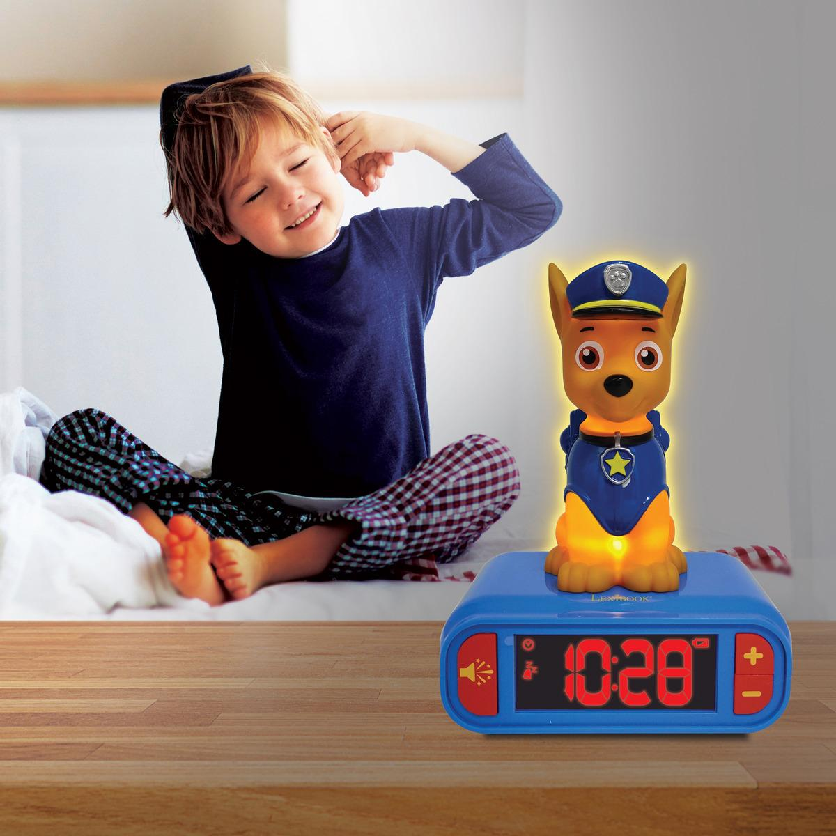 Junge in Pyjama dehnt sich neben einem Paw Patrol Wecker mit leuchtender Chase-Figur.