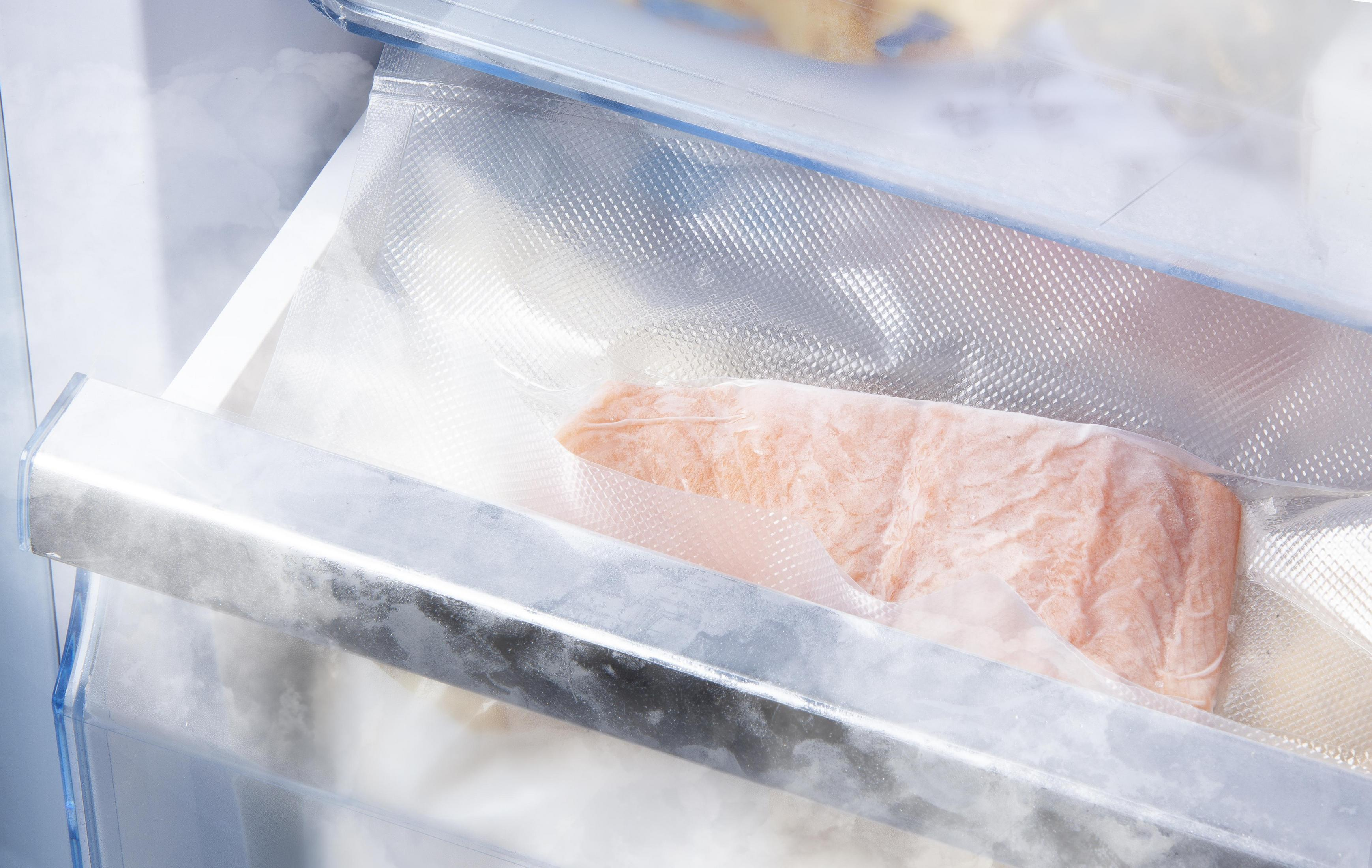 Eine Kühlschublade mit einem vakuumversiegelten Beutel, der ein Lachsfilet enthält. Hintergrund zeigt Gefrierelemente.