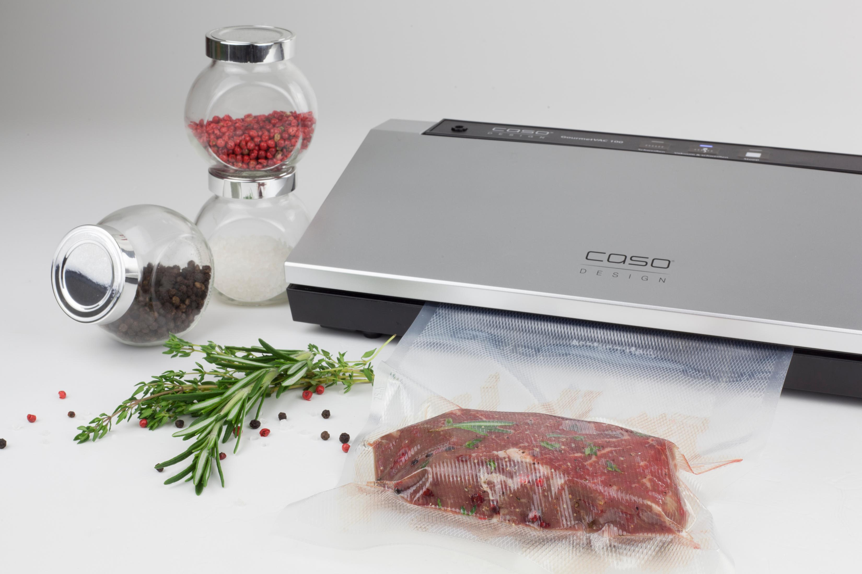 Sigillatrice sottovuoto con confezione di carne ed erbe aromatiche. Vasetti di vetro con spezie ed erbe accanto.
