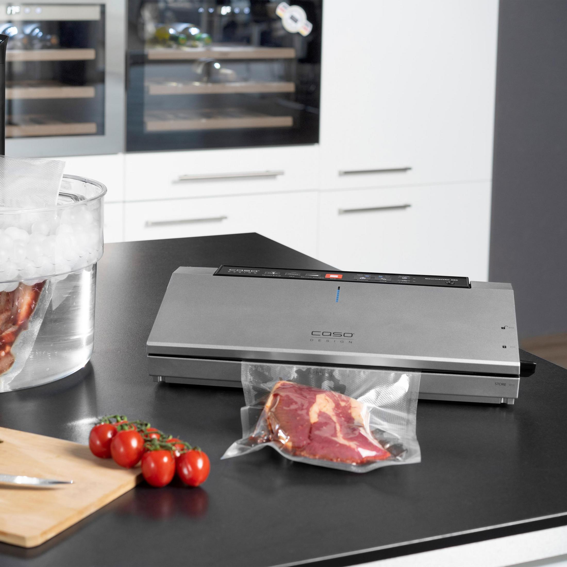 Ein Vakuumiergerät, Tomaten und eine Tüte Fleisch auf einer schwarzen Theke in der Küche.