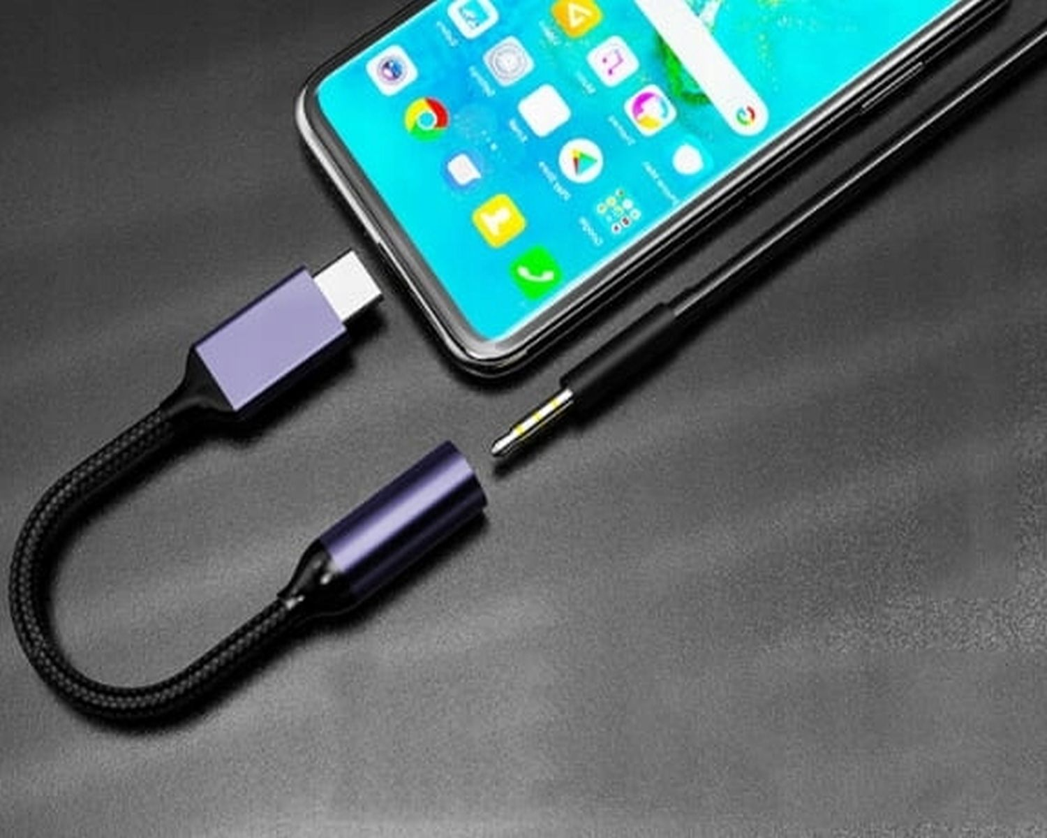 Adapter audio USB-C do 3,5 mm, podłączony do smartfona. Telefon jest niebieski.