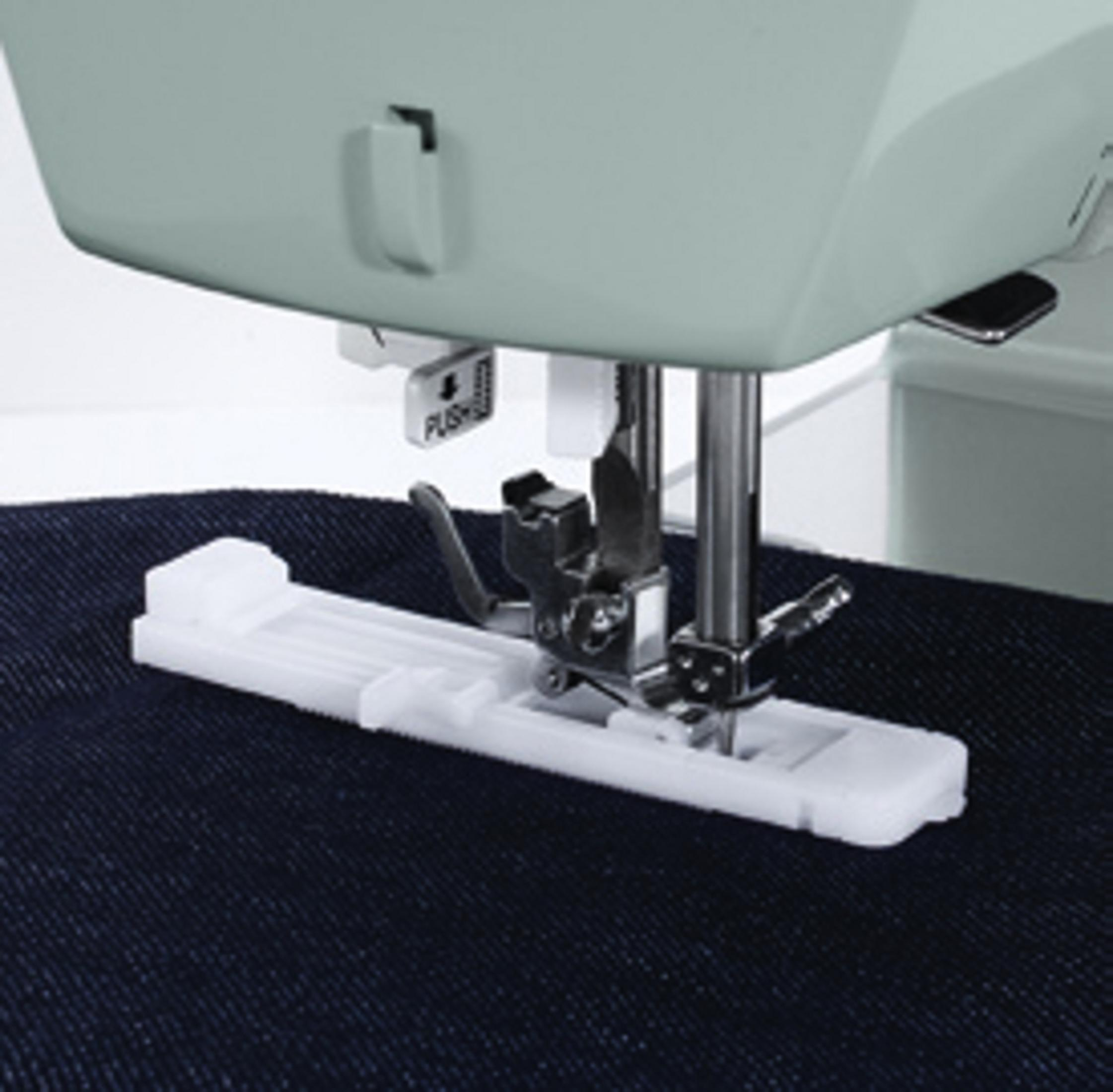 Stopka maszyny do szycia znajduje się nad ciemnym materiałem. Stopka jest biała i ma przystawkę do dziurek na guziki.