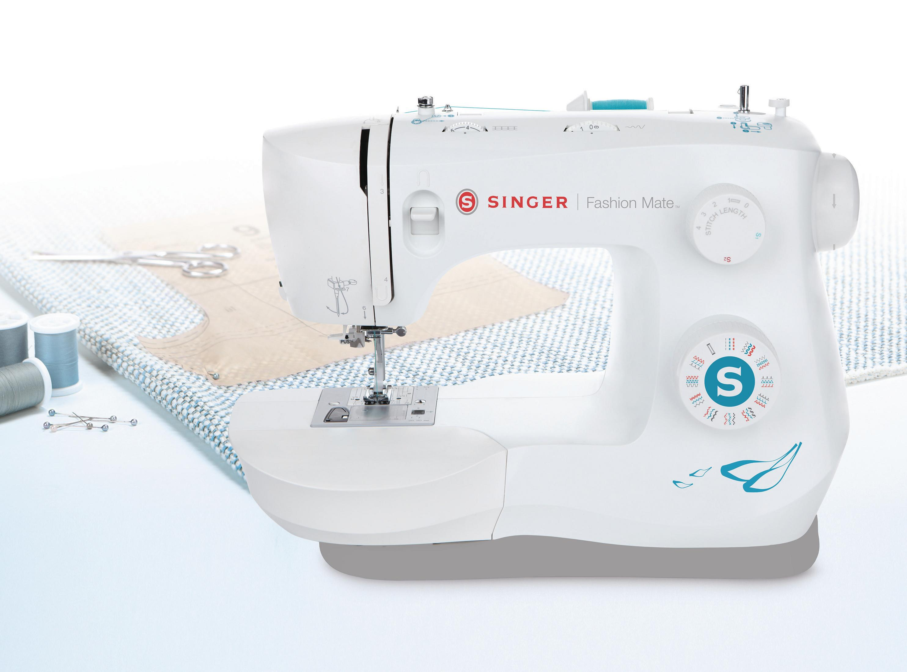 Biała maszyna do szycia Singer z niebieskimi akcentami, tkaniną i narzędziami na białej powierzchni.