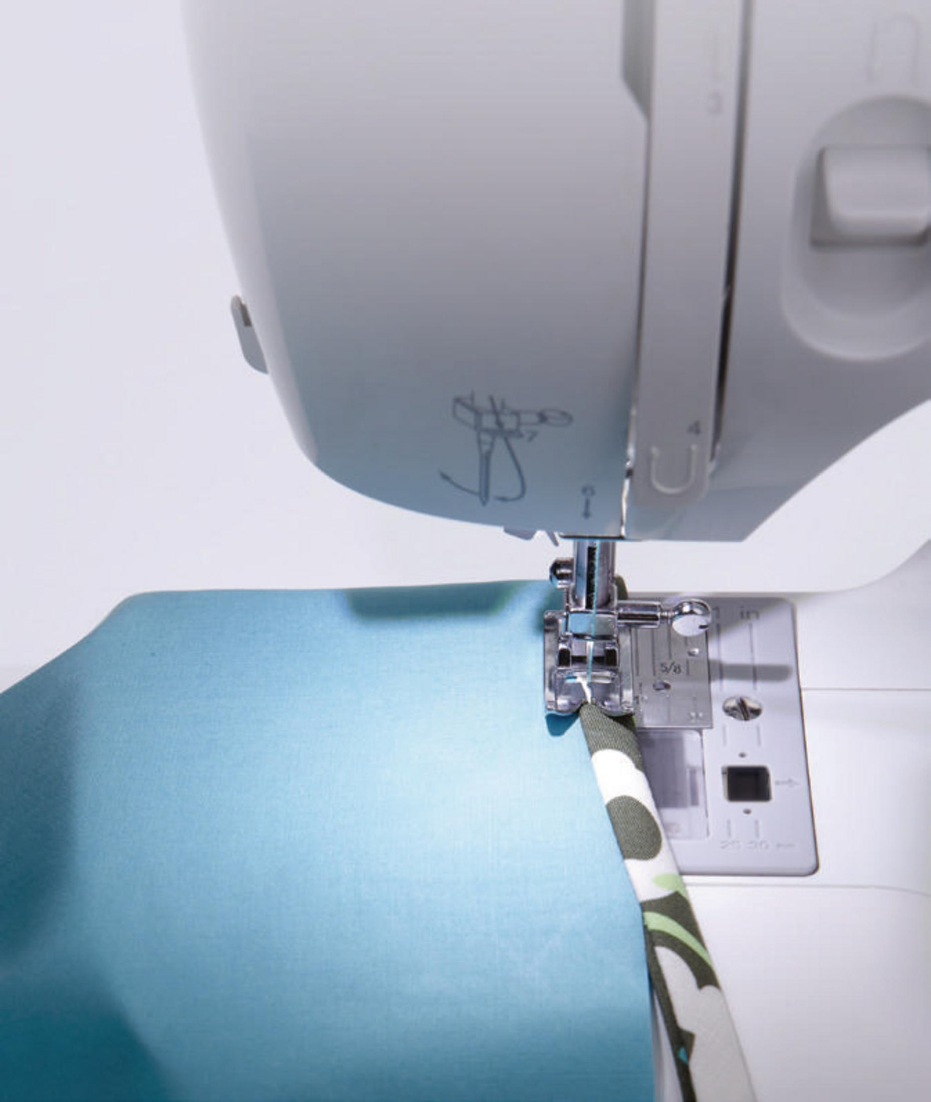 Igła maszyny do szycia szyjąca niebieską tkaninę z wzorzystą krawędzią.