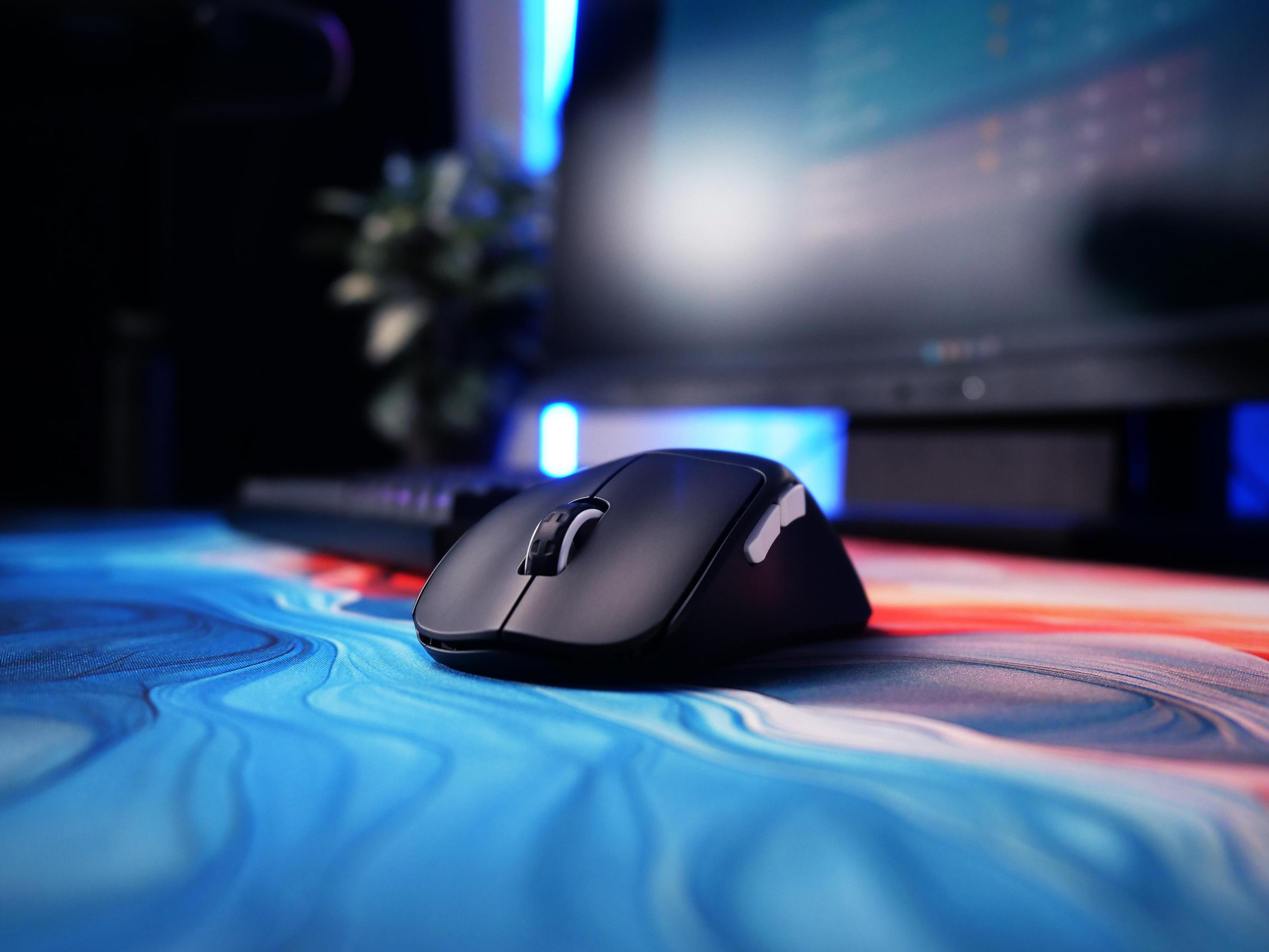 Mouse per computer nero su un tappetino colorato. Tastiera e monitor sullo sfondo.