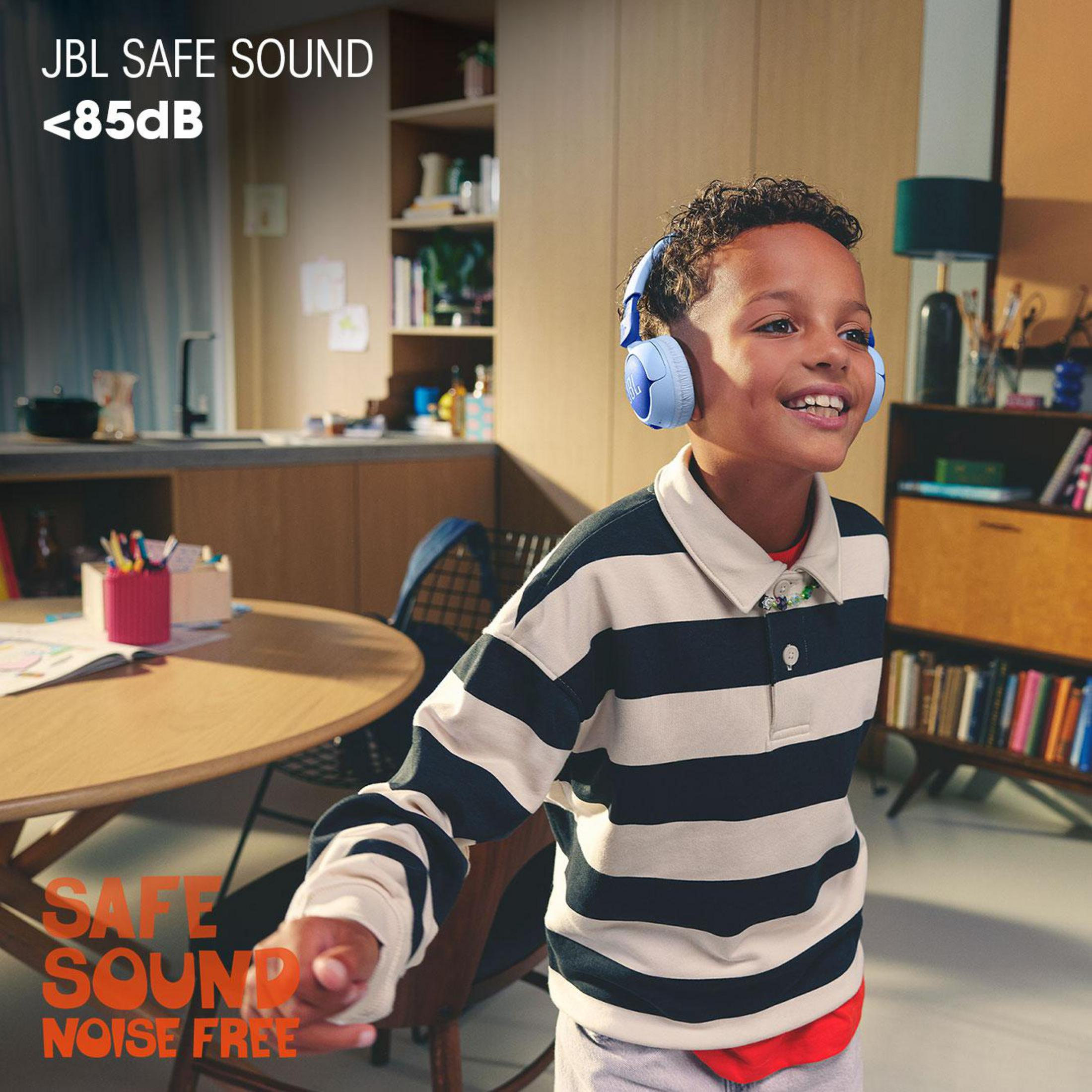 Ragazzo con cuffie che sorride in una stanza. JBL Safe Sound. Camicia a righe.