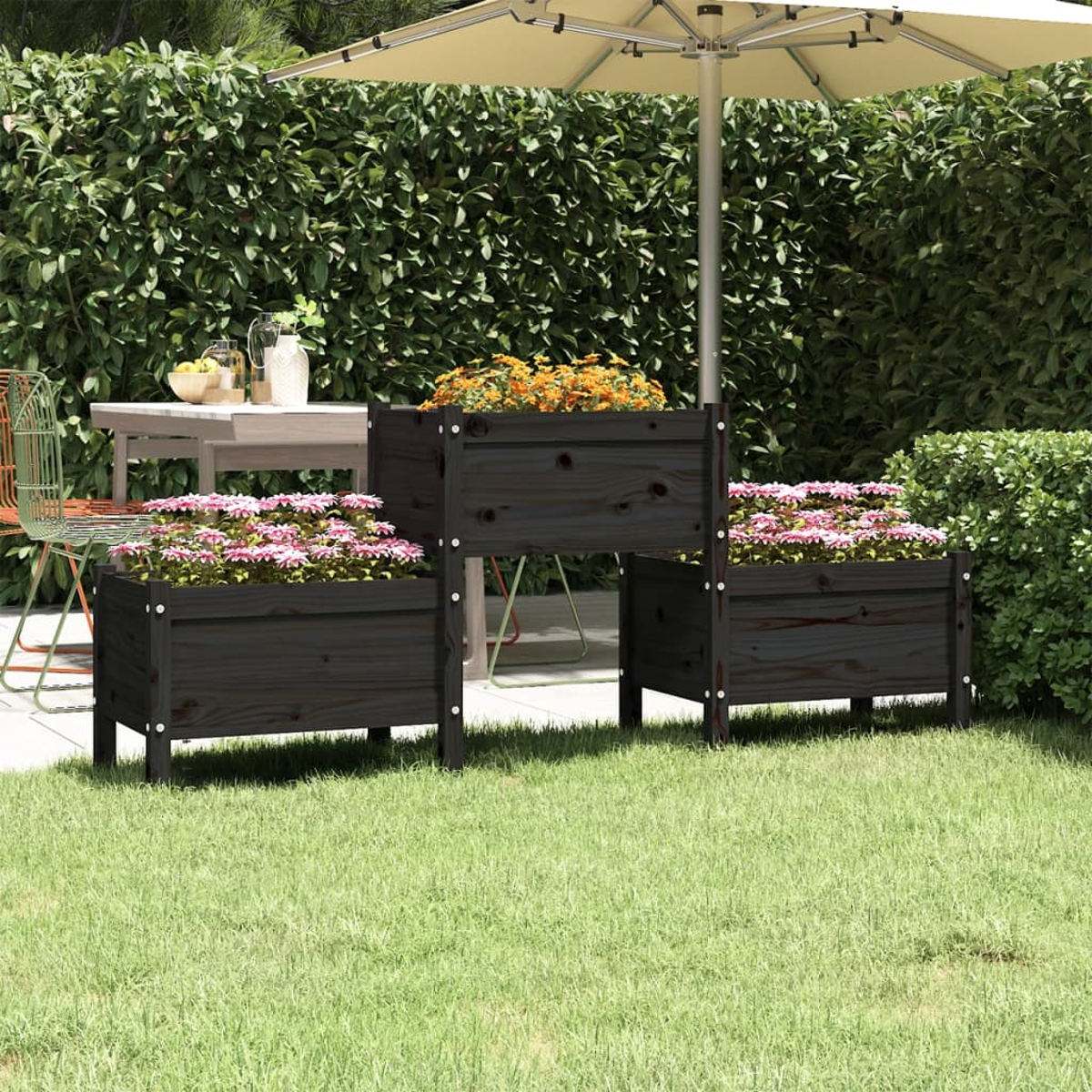 Drei Pflanzkübel aus dunklem Holz mit rosa und orangefarbenen Blumen auf einem grünen Rasen, im Hintergrund ein Tisch und Schirm.