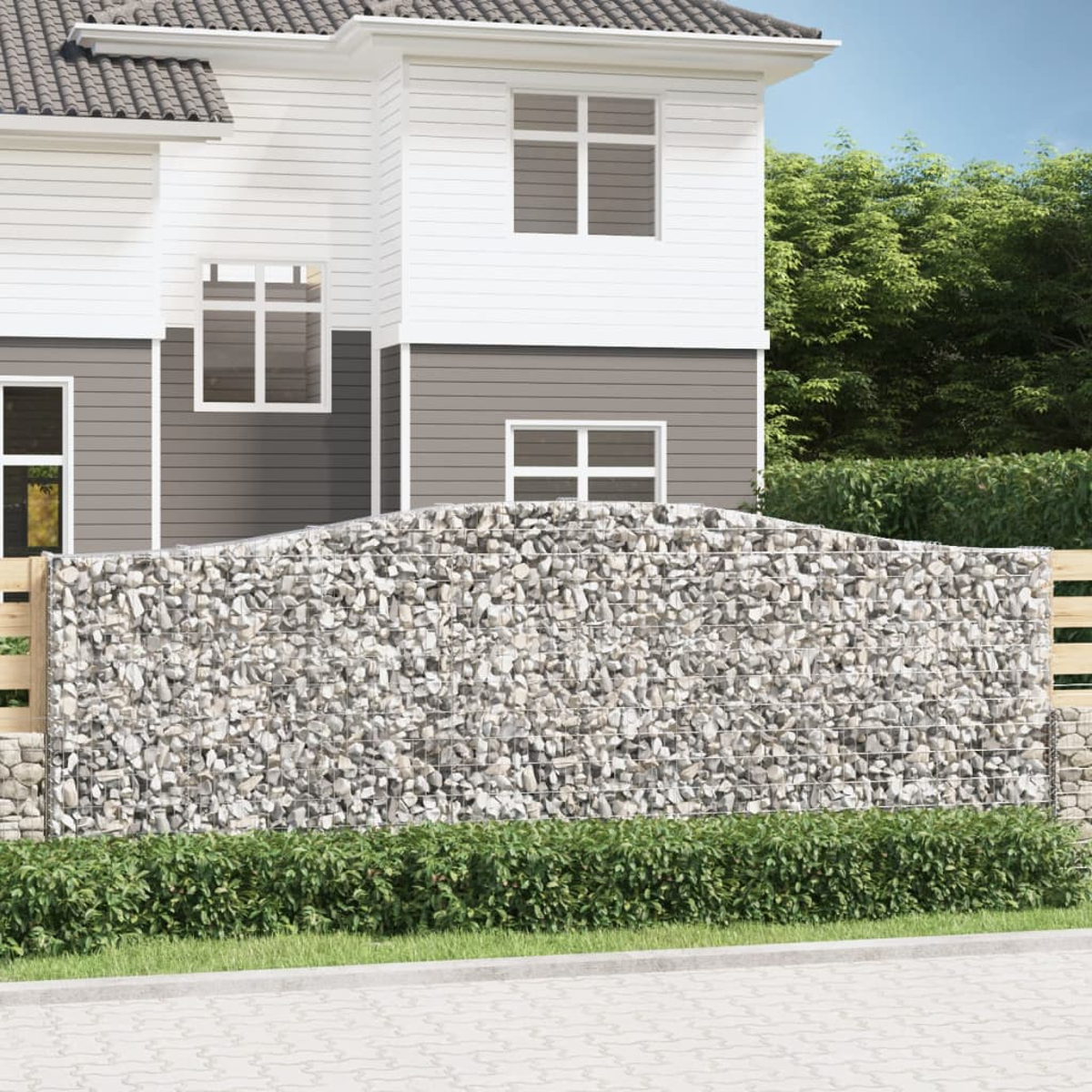 Ein Haus mit Steinmauer davor. Grüne Büsche und blauer Himmel im Hintergrund.