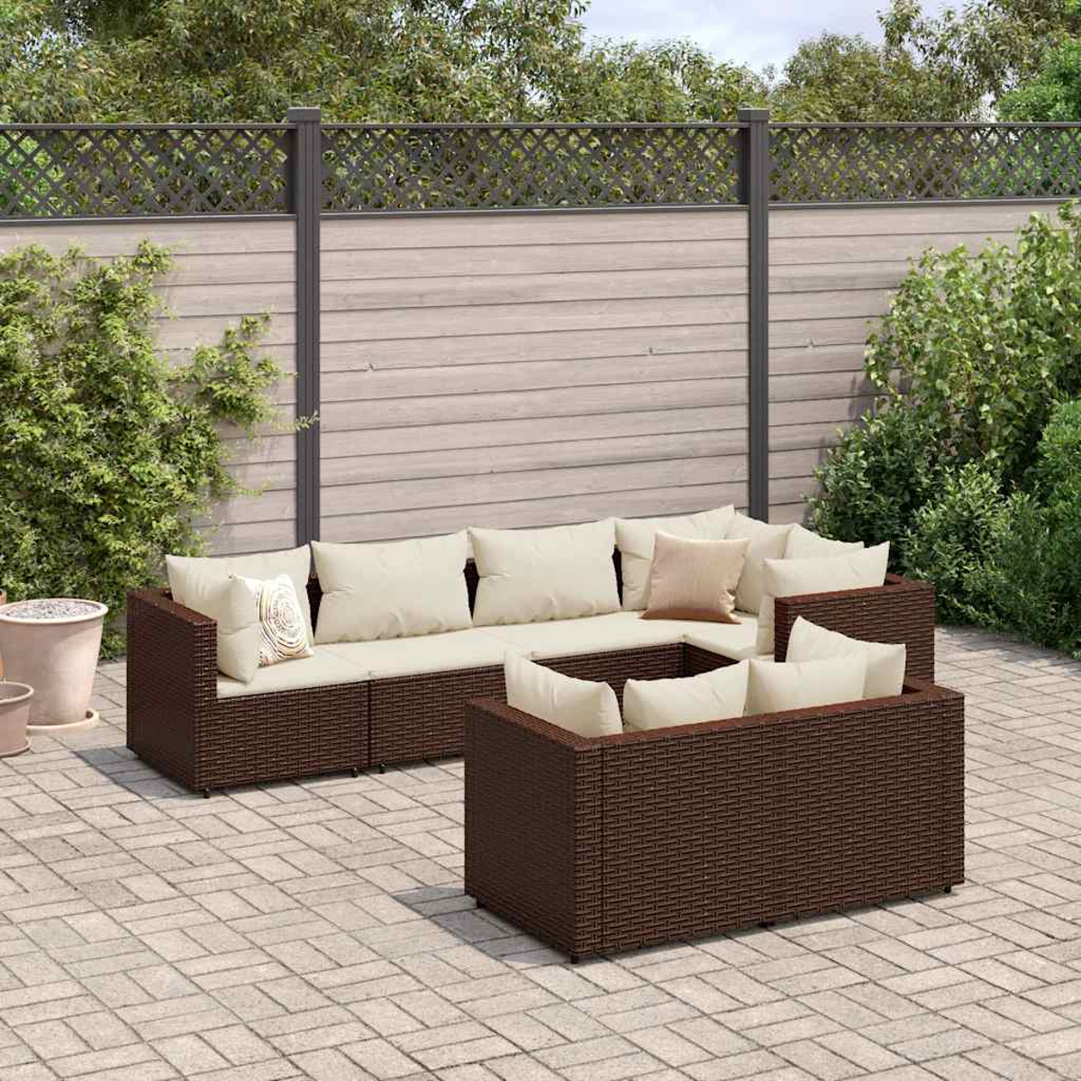 Sofá seccional de ratán marrón en un patio pavimentado con valla de madera y fondo verde.