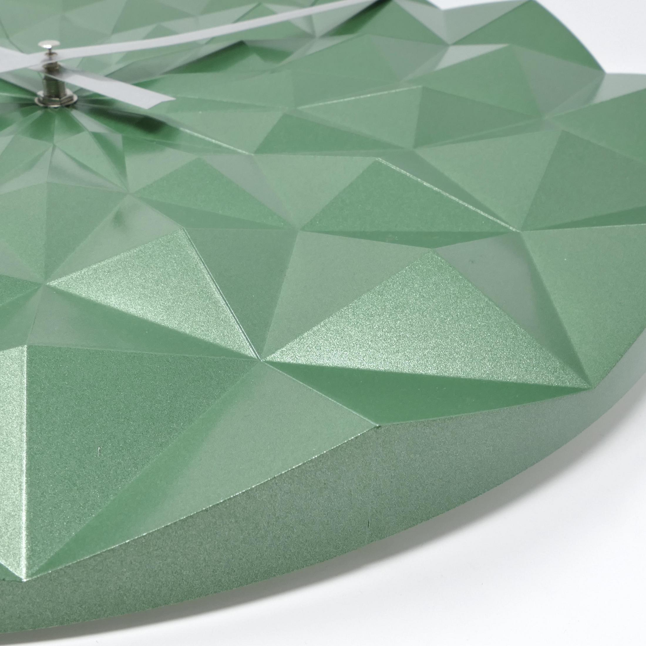 Nahaufnahme einer grünen, geometrischen Uhr mit dreieckigen Formen. Die Zeiger sind silberfarben.