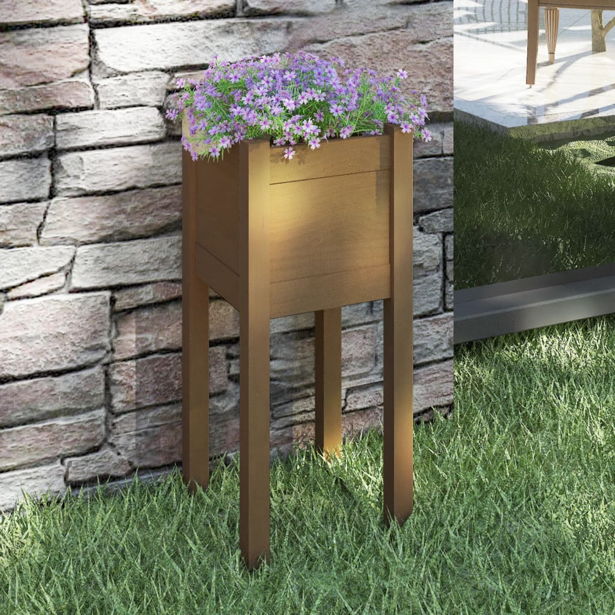 Hoher Holzpflanzer mit lila Blumen. Steht auf Gras, vor einer Backsteinmauer.