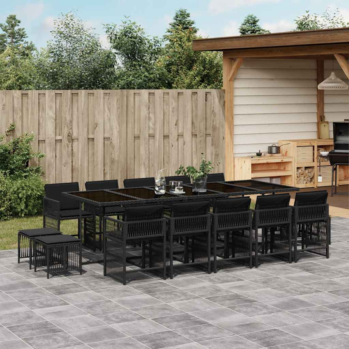 Schwarzes Ess-Set für den Außenbereich mit Tisch, Stühlen und Hockern auf einer Terrasse mit Holzzaun im Hintergrund.