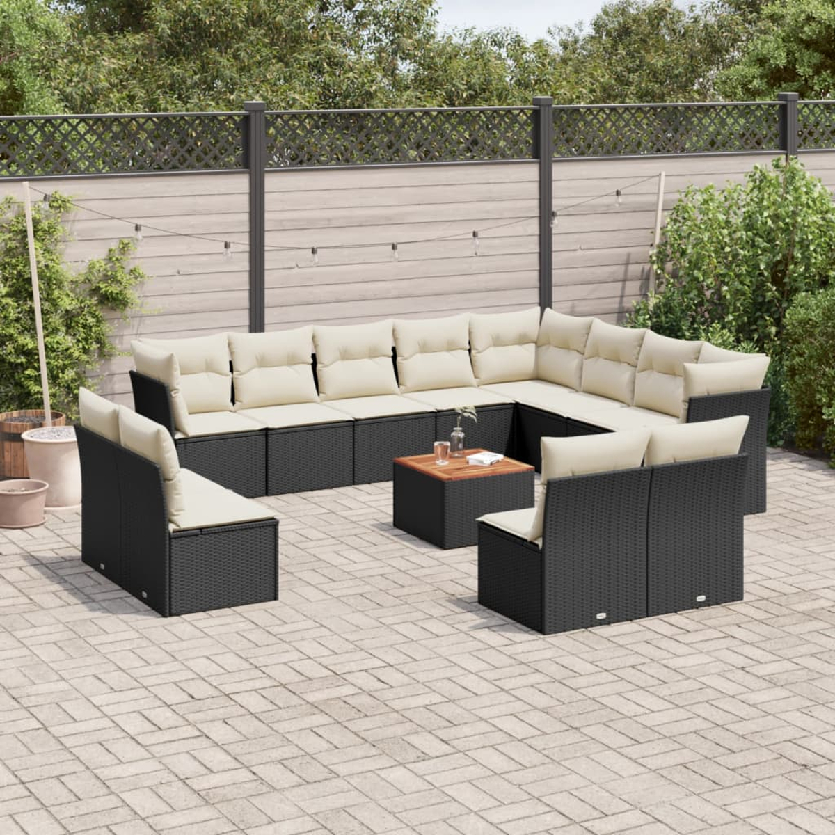 Schwarzes Ecksofa aus Korbgeflecht mit cremefarbenen Kissen, Couchtisch. Außenbereich mit Pflanzen.