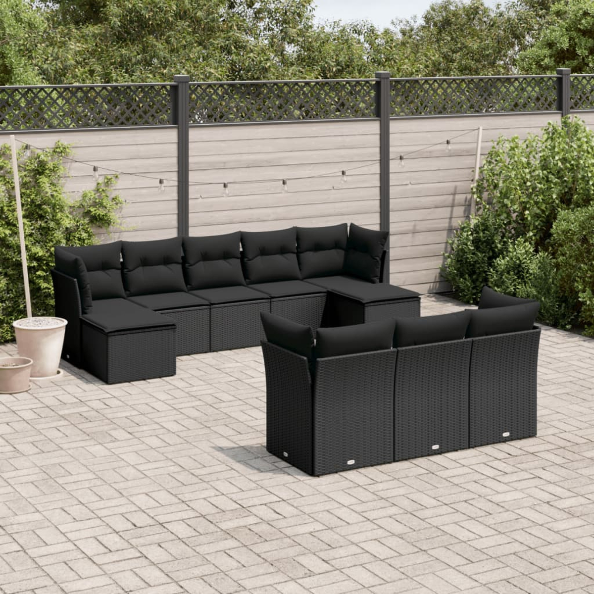 Schwarzes Outdoor-Sofa aus Korbgeflecht auf Ziegelpflaster. Mit Tisch und Grün.
