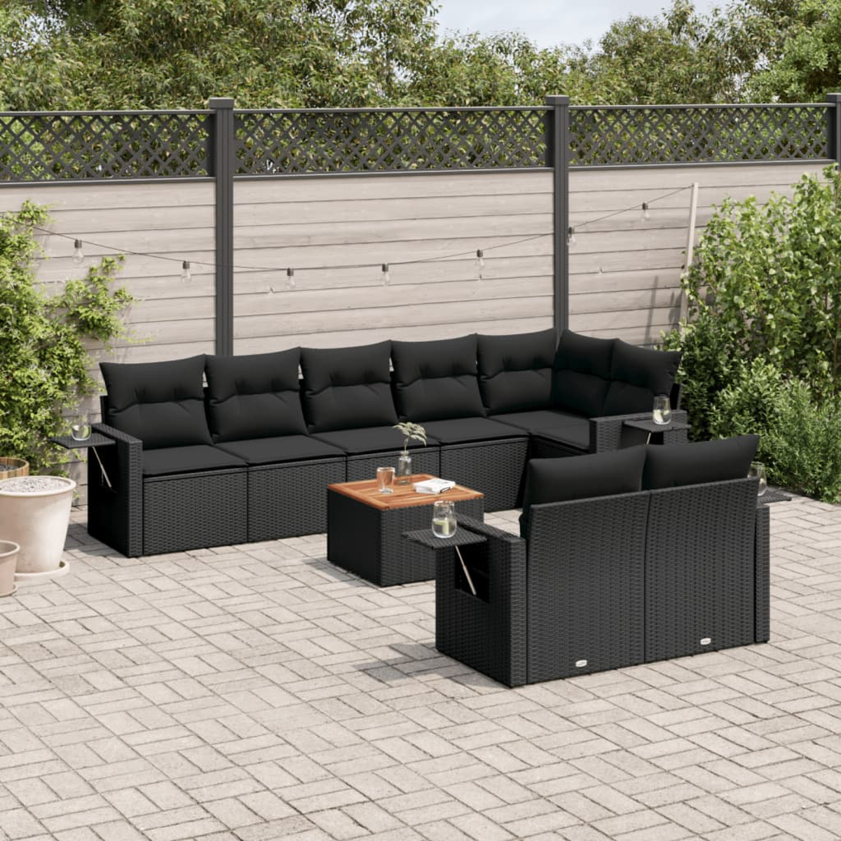 Divano angolare da esterno in rattan nero con cuscini, tavolo e sfondo giardino.