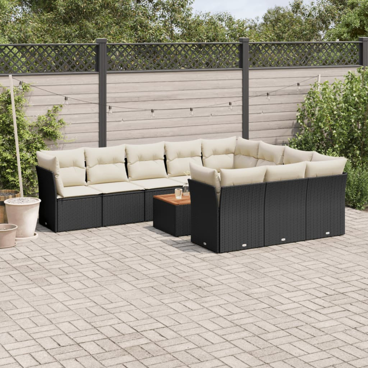 Outdoor-Setting mit schwarzem Sofaset, einem Holztisch und einem gepflasterten Bereich.