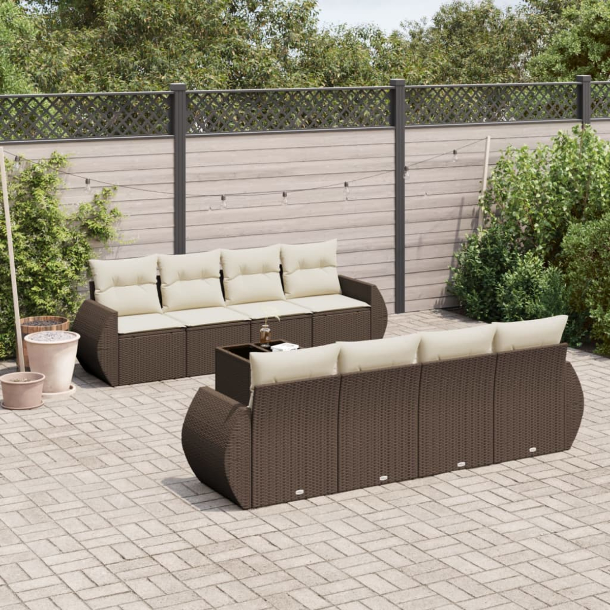 Set di divani in vimini marrone per esterni con cuscini beige. Il set è su un patio in mattoni con una recinzione sullo sfondo.