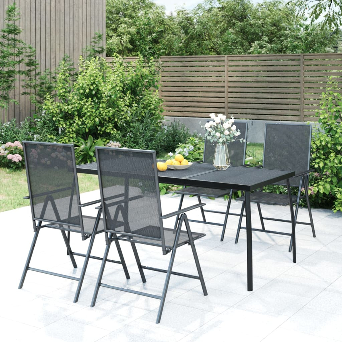Schwarzer Metalltisch mit Netzstühlen im Garten. Blumen und Zitronen auf dem Tisch.