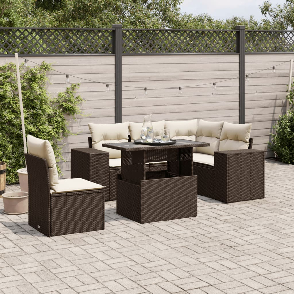Dunkelbraunes Korbgartenmöbel-Set mit Tisch und Stühlen. Cremefarbene Kissen und Gläser.