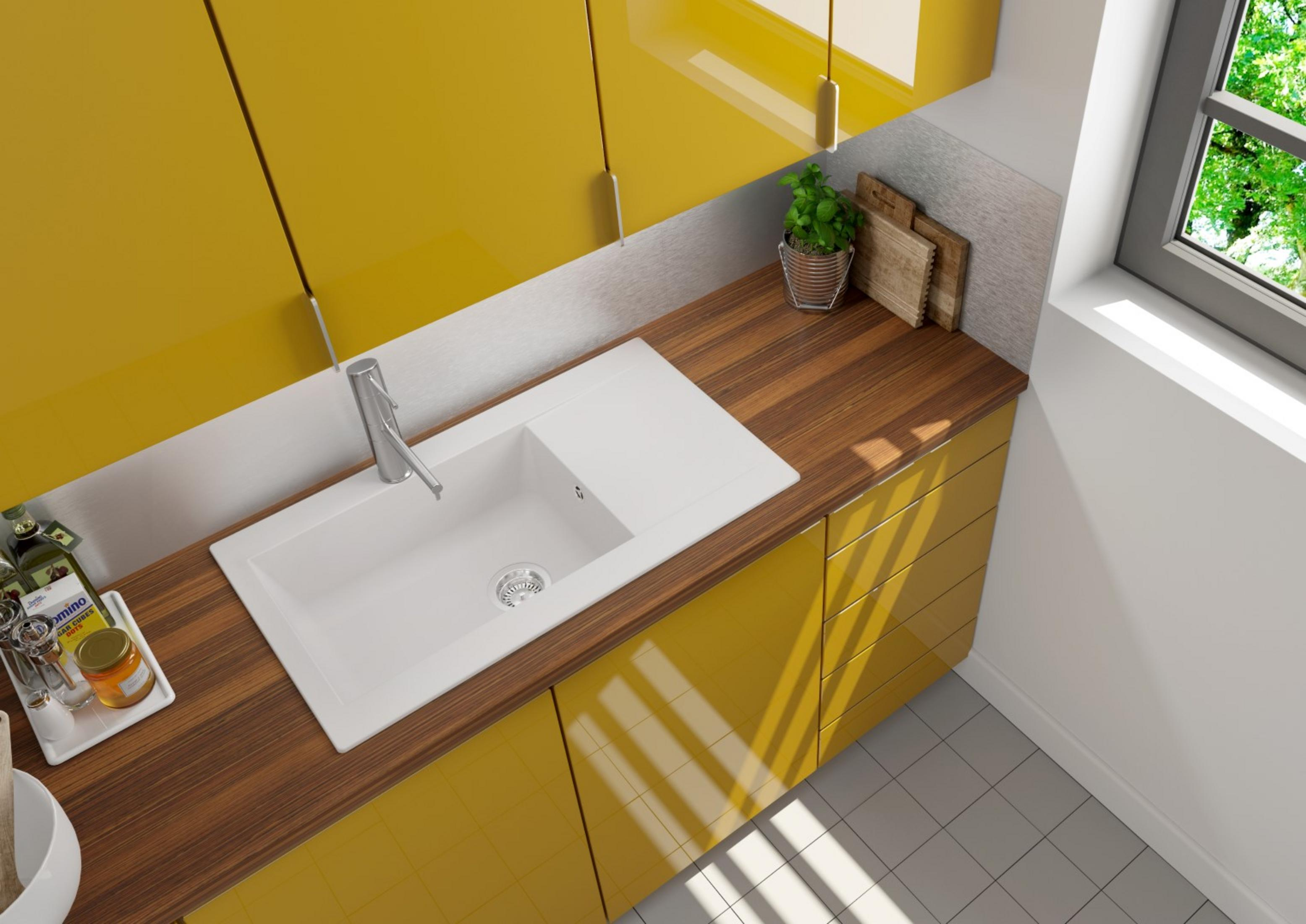 Küchentheke mit gelben Schränken und einem weißen Waschbecken. Im Hintergrund ein Fenster und eine Pflanze.