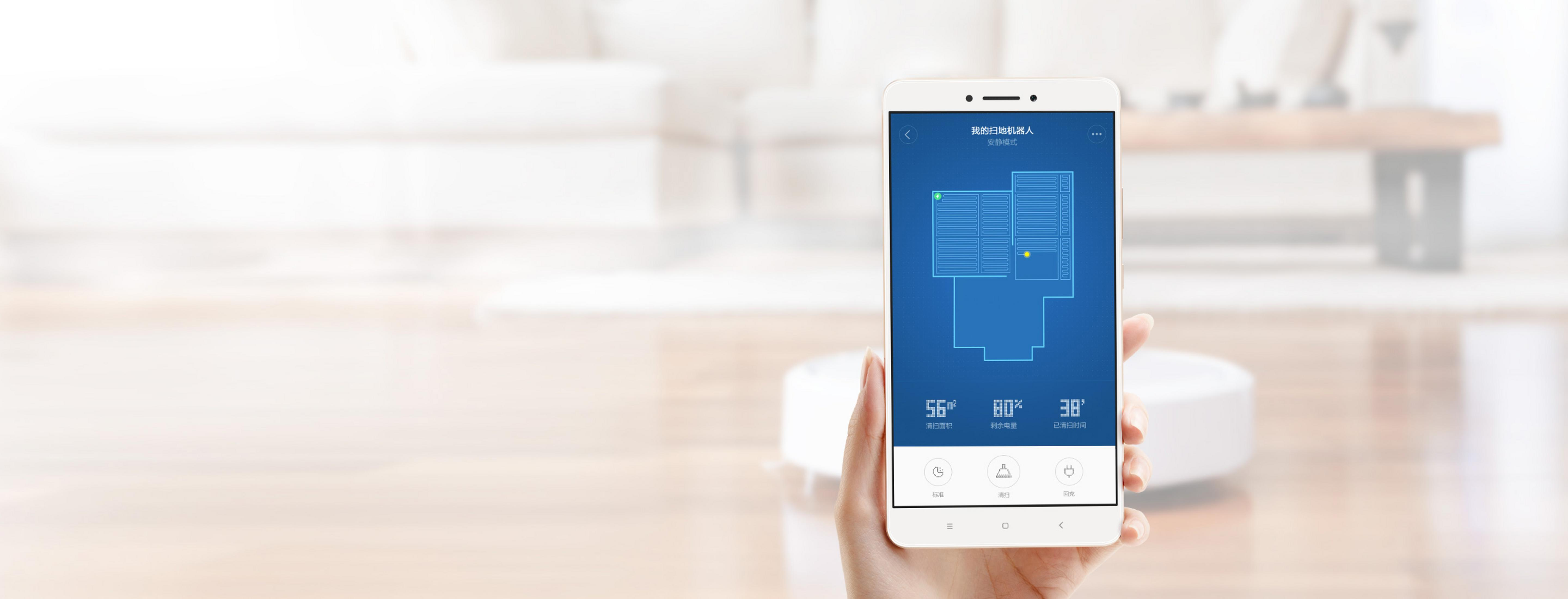 Ein Smartphone zeigt eine Raumkarte. Ein Roboter-Reiniger ist im Hintergrund, auf einem Holzboden.