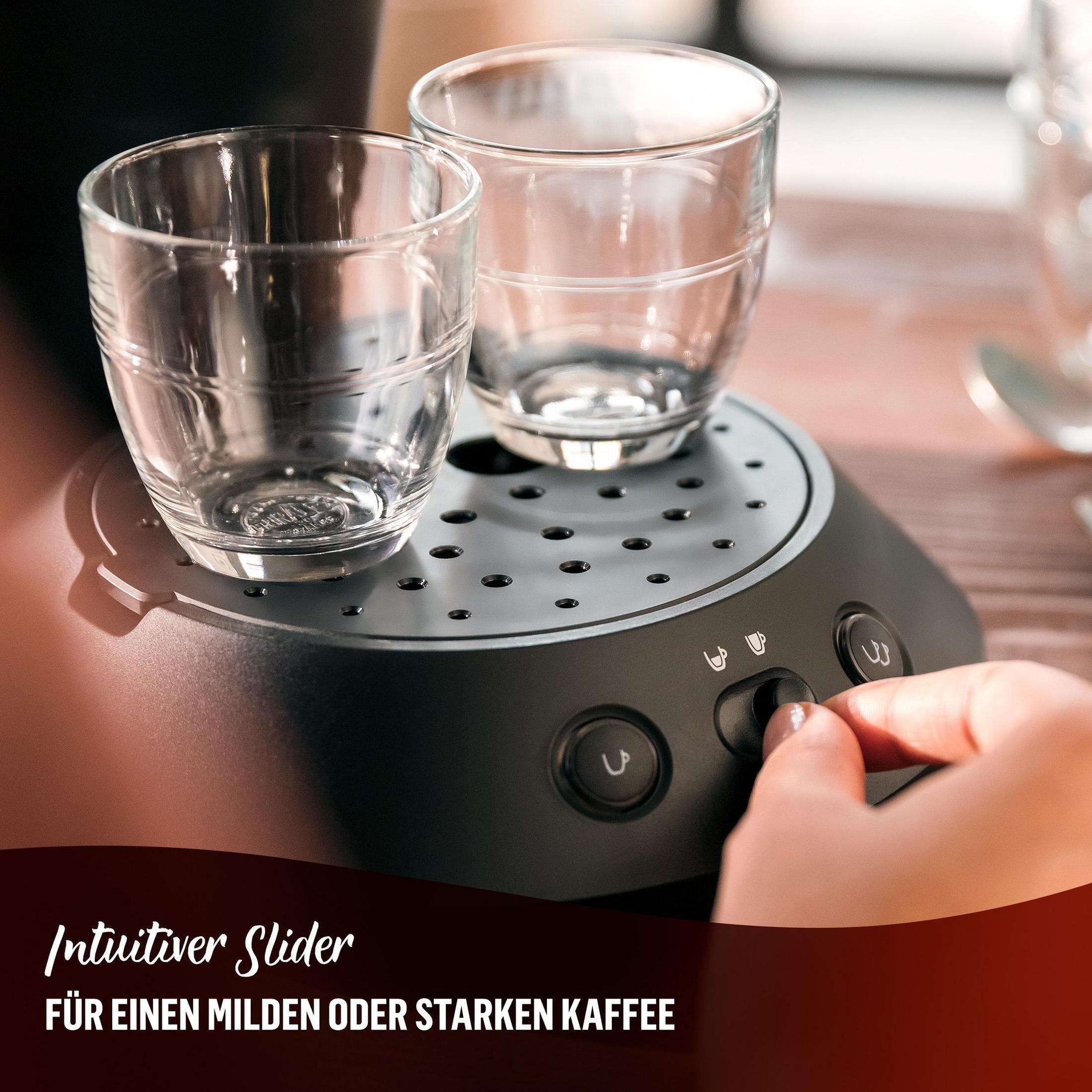 Hand drückt Knopf an Kaffeemaschine. Zwei Gläser sind vorhanden.