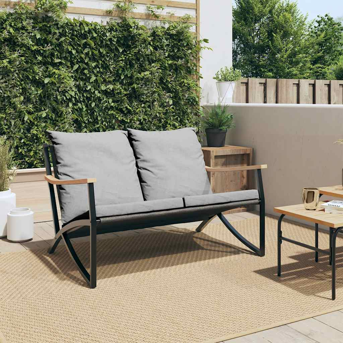 Outdoor-Zweisitzer mit grauen Kissen und Holzarmlehnen. Auf einem gewebten Teppich.