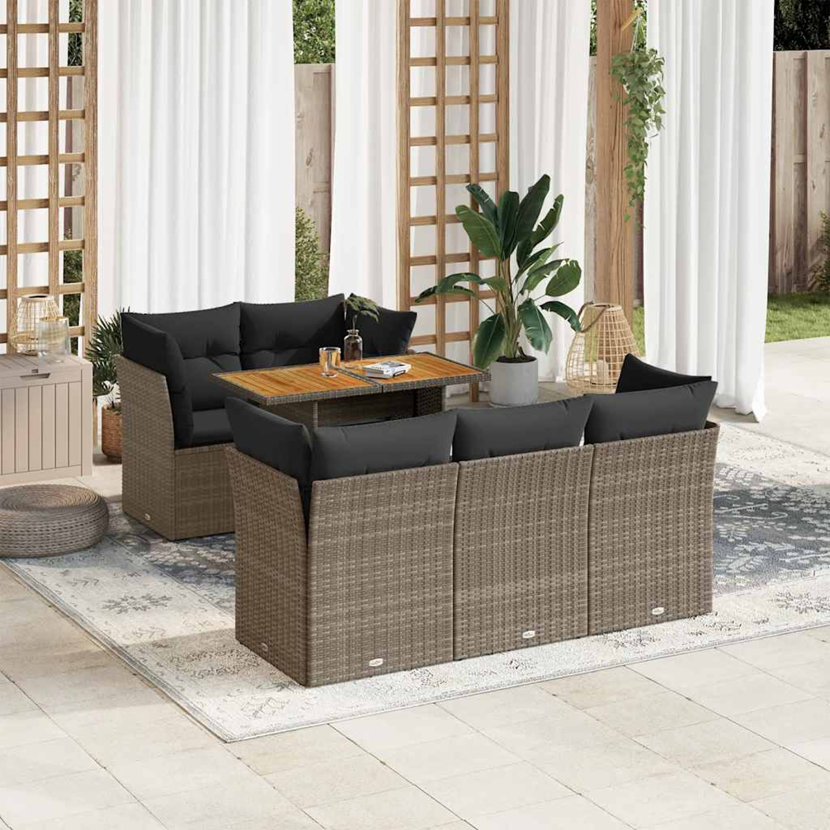 Set di mobili da esterno in vimini con cuscini neri, tavolo, piante e tappeto, su un patio.