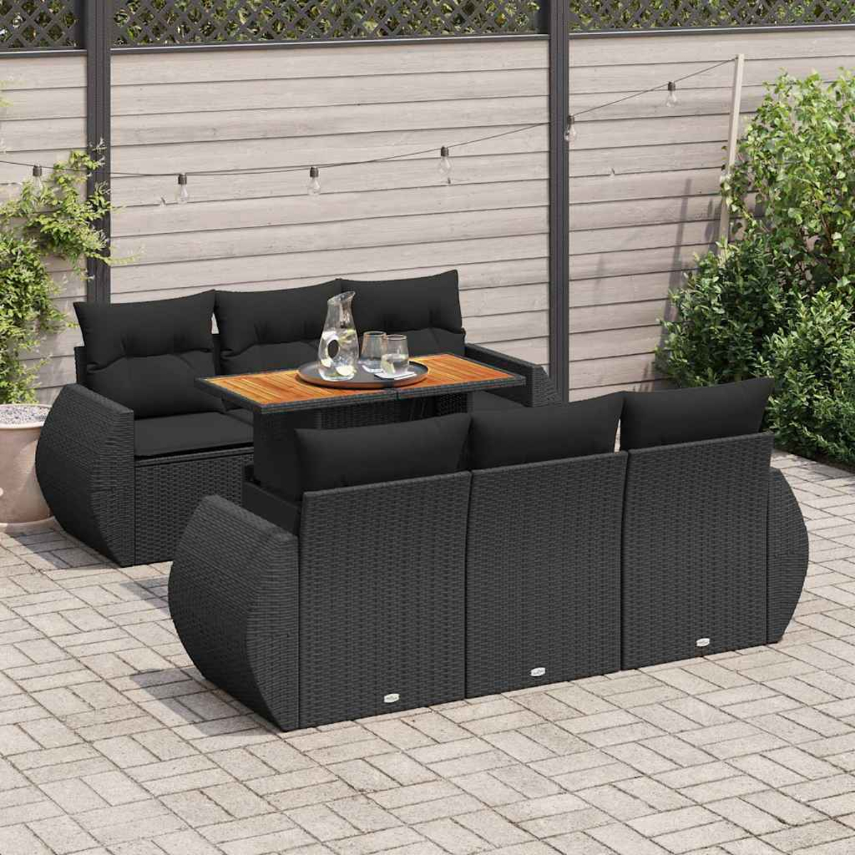Set di mobili da esterno in vimini nero con cuscini neri e un tavolo in legno.