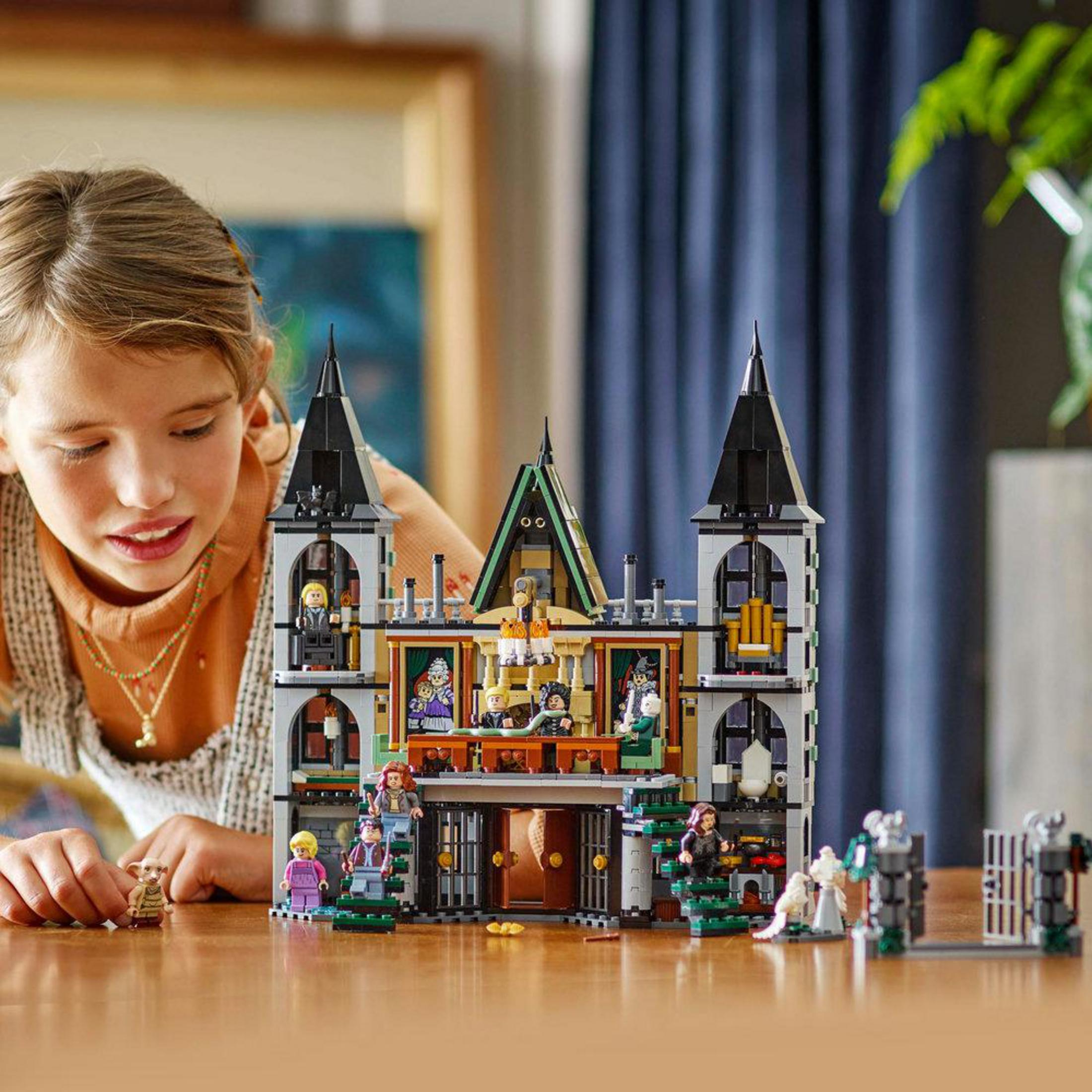 Una ragazza che gioca con un set Lego Harry Potter Malfoy Manor su un tavolo di legno.