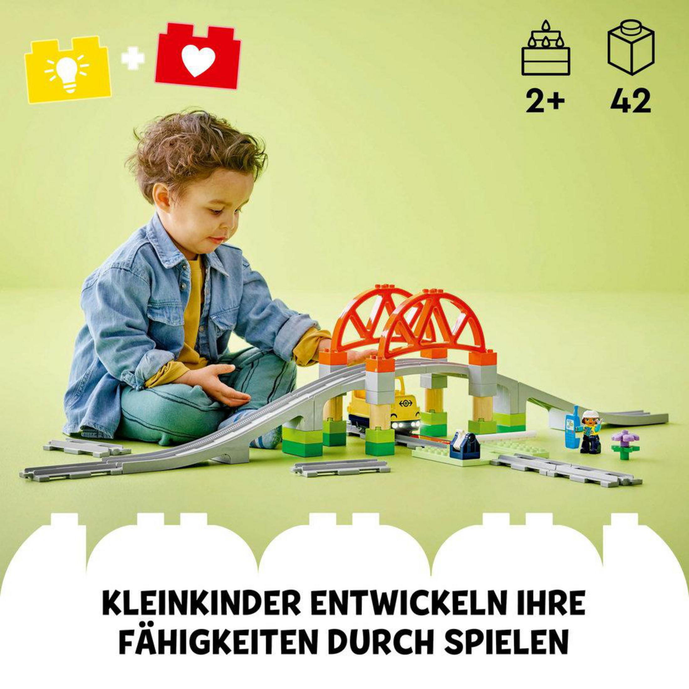 Un bambino gioca con un set di treni Lego Duplo con ponte.