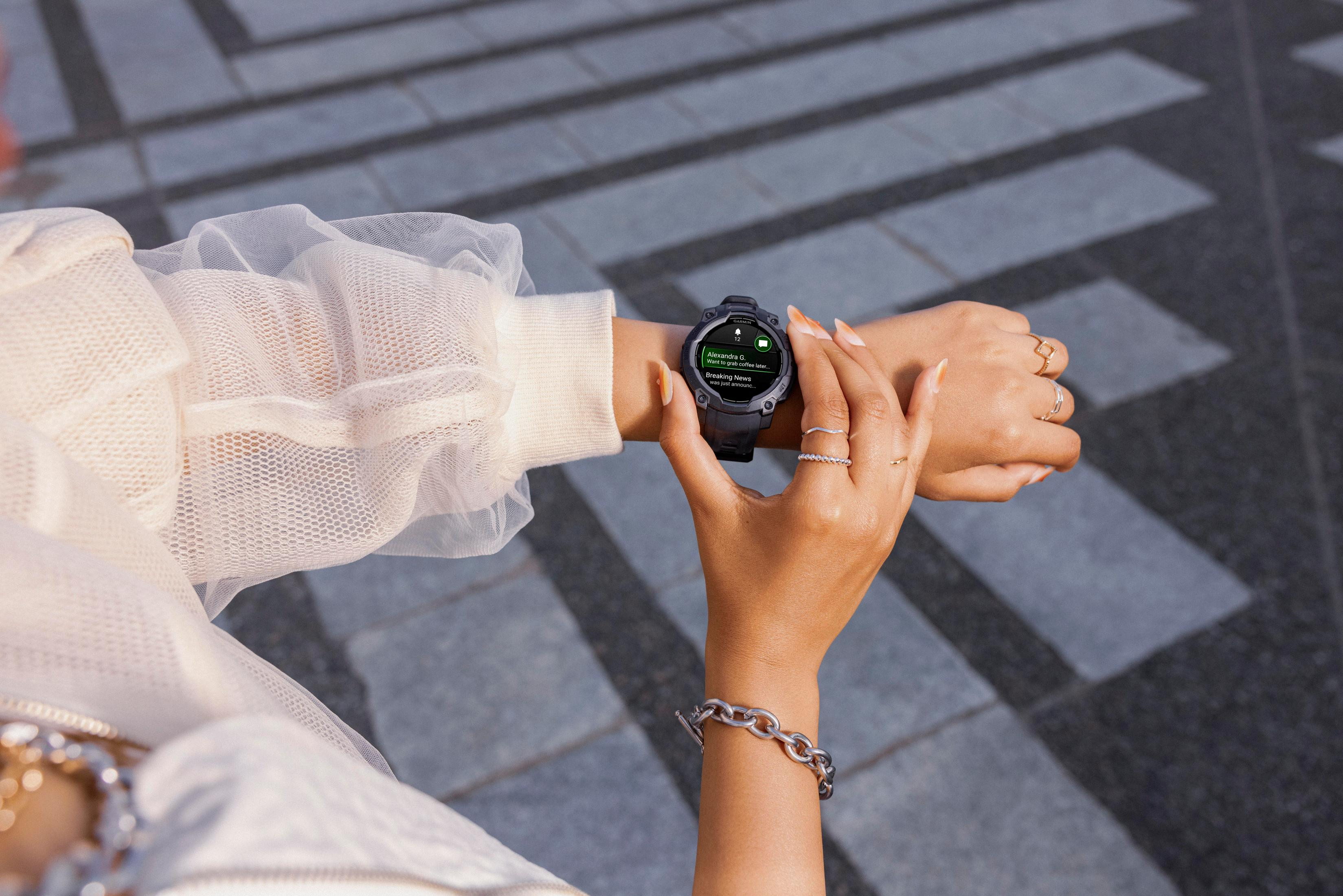 Das Handgelenk einer Frau mit einer schwarzen Smartwatch. Sie berührt sie, in einer urbanen Umgebung mit Pflastersteinen.