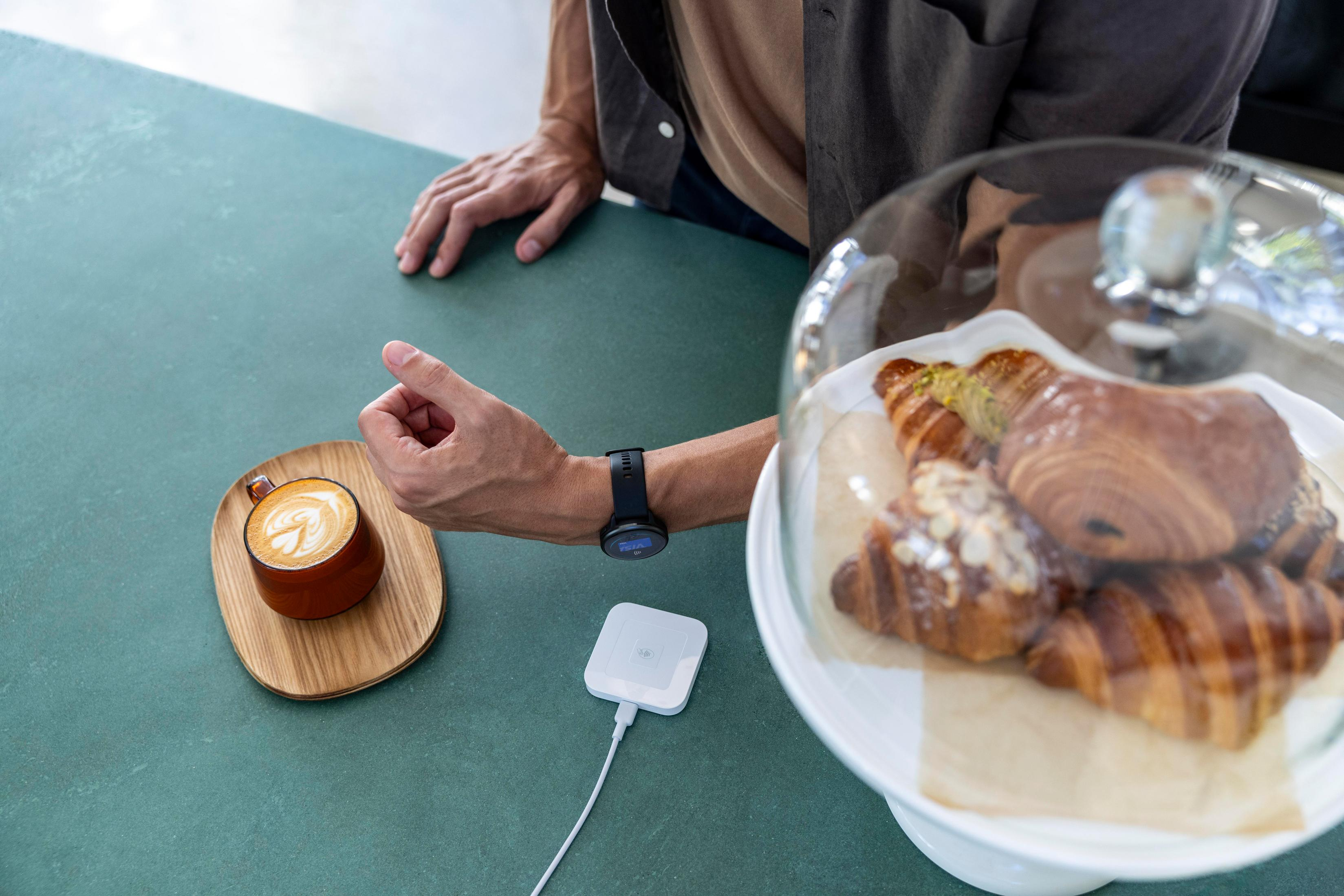 Ramię ze smartwatchem, kawa i ciastka na stole w kawiarni.