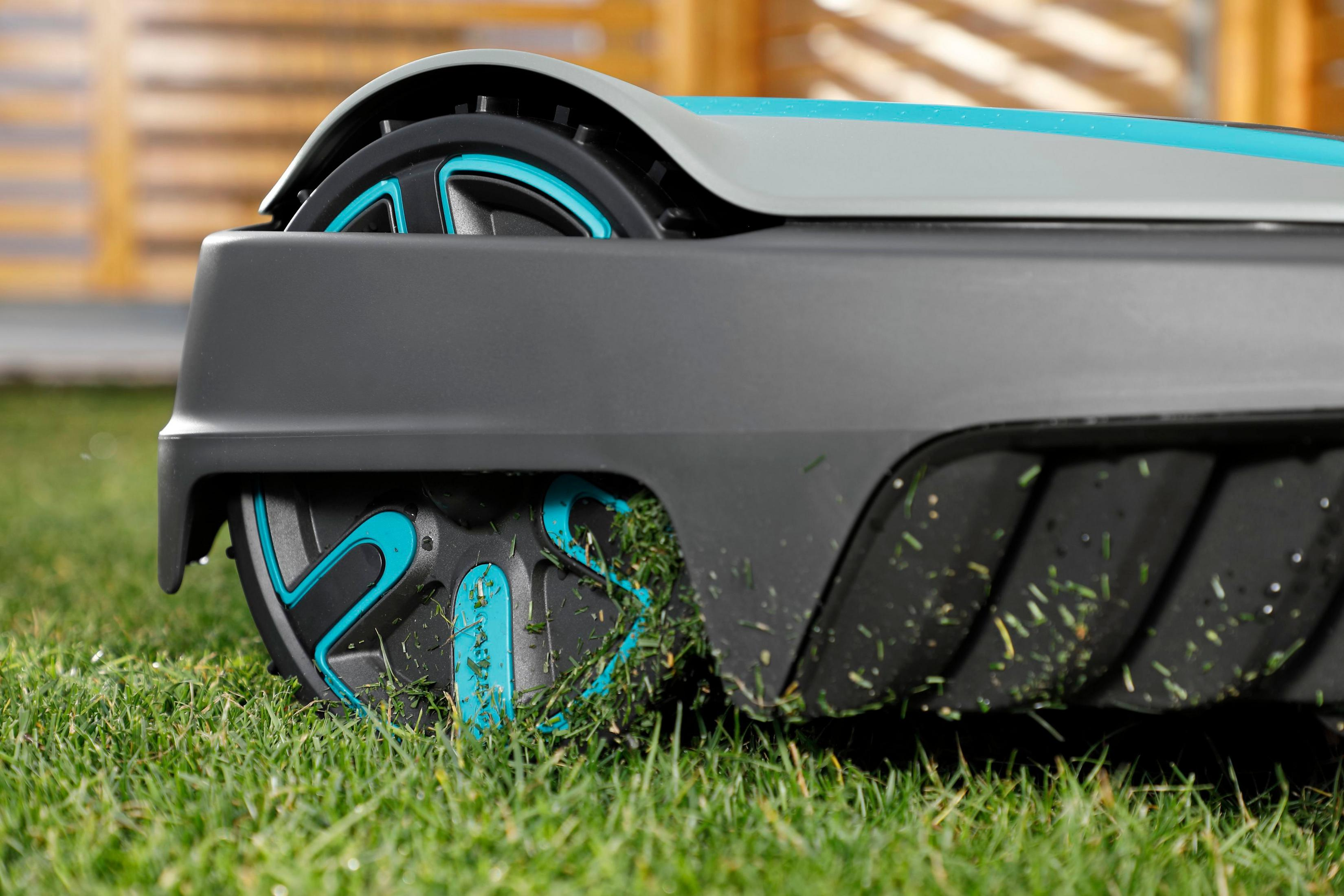Rad eines Rasenroboters, graue und tealfarbene Akzente, schneidet Gras auf grünem Rasen.