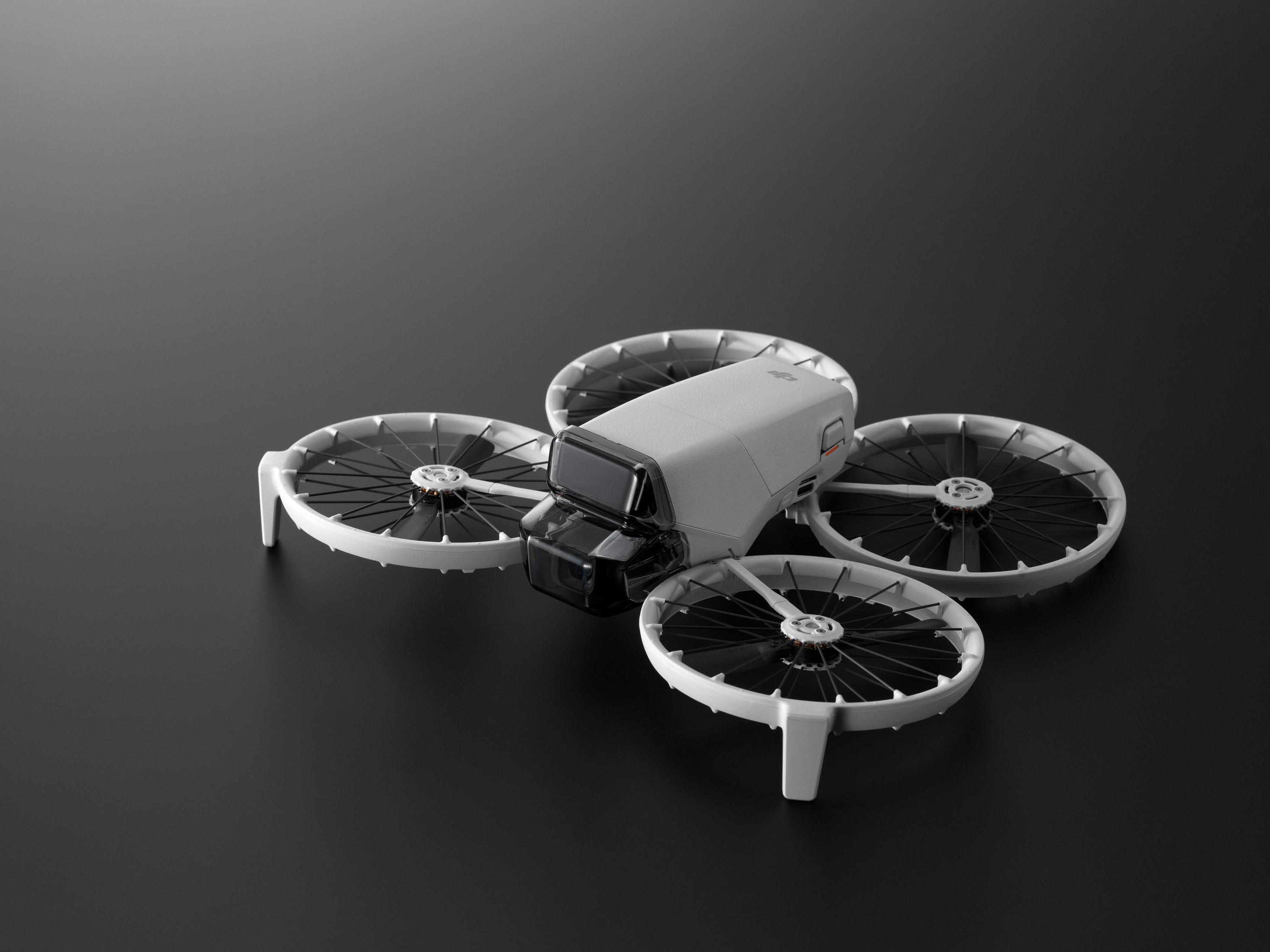 Un dron blanco con cuatro hélices sobre una superficie oscura. El dron tiene una cámara y está orientado al espectador.