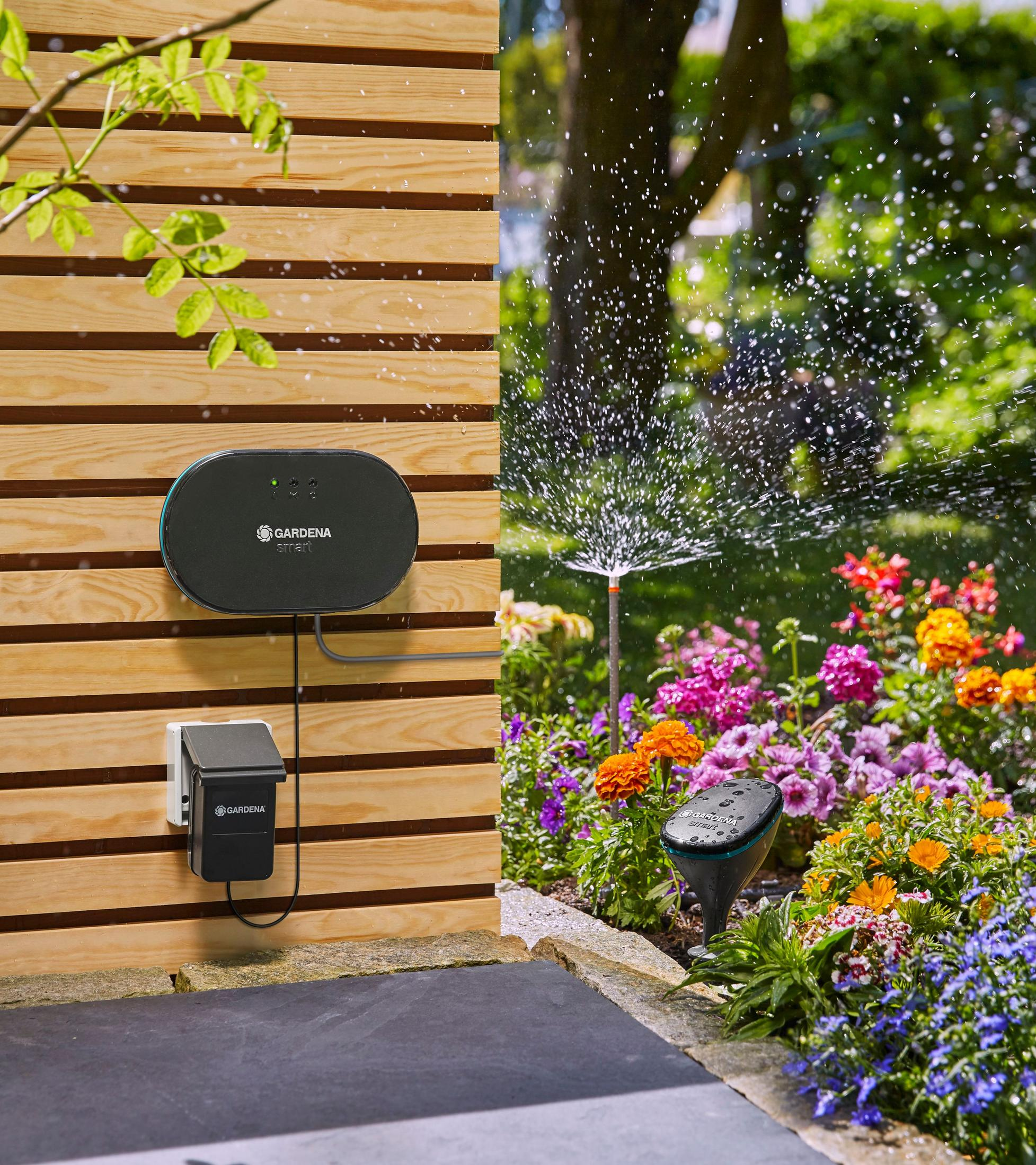 Inteligentny system nawadniania domu zamontowany na panelach drewnianych. Zraszacz w ogrodzie z kolorowymi kwiatami.