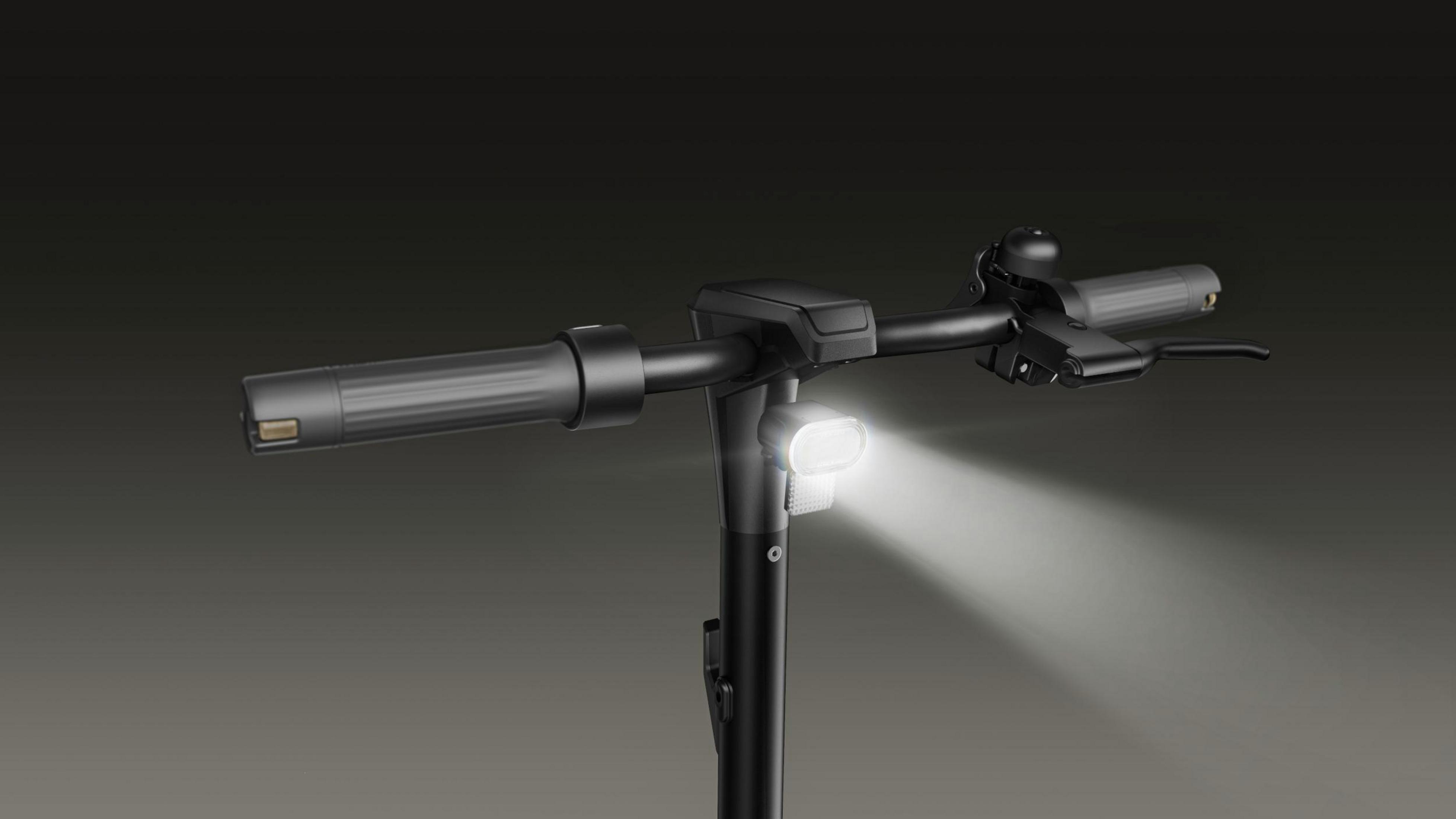 Nahaufnahme des Lenkers eines E-Scooters mit hellem Scheinwerferstrahl. Schwarze und graue Töne dominieren die Szene.