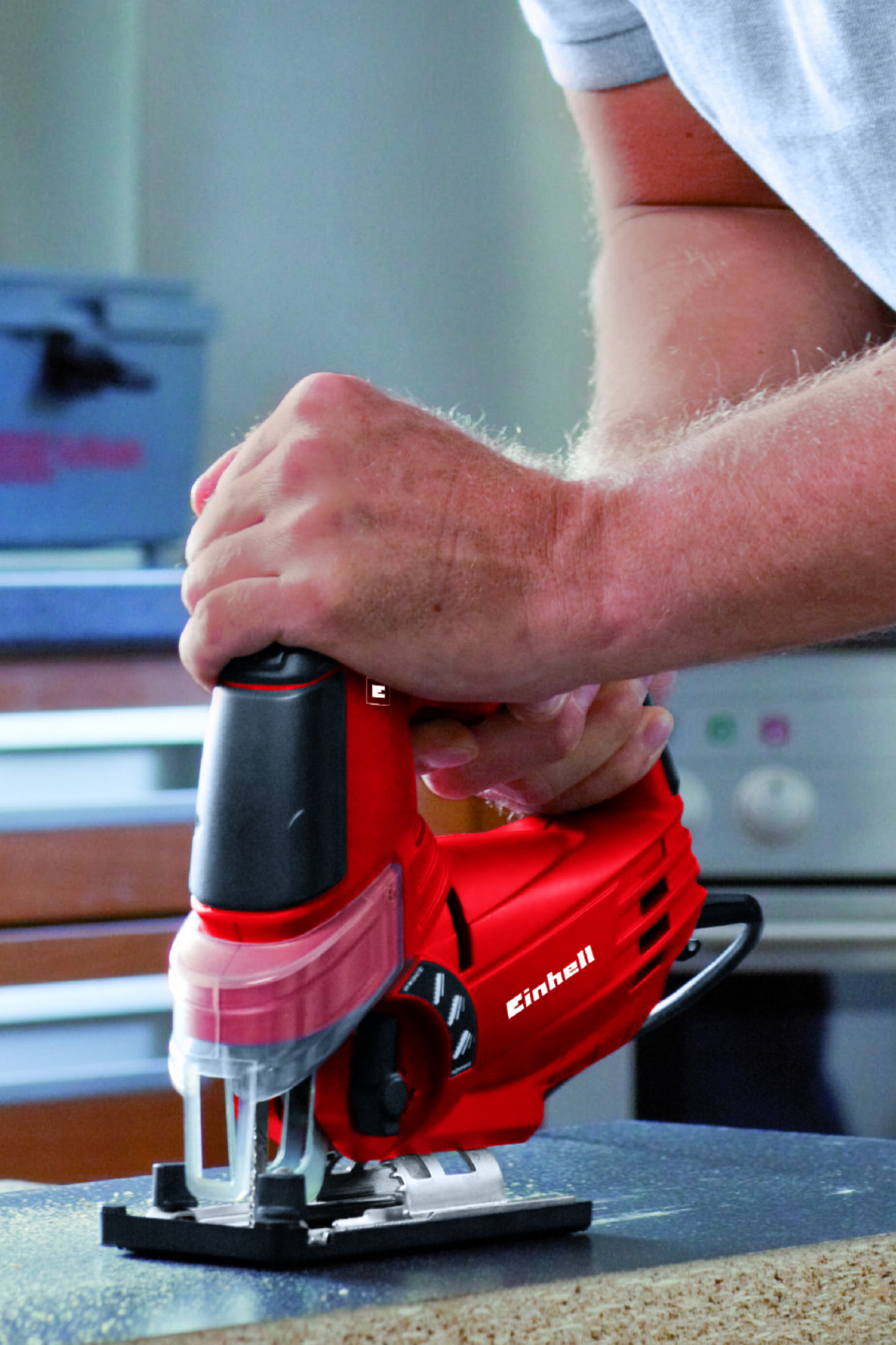 Osoba trzymająca czerwoną wyrzynarkę Einhell, pracująca na drewnianej powierzchni.