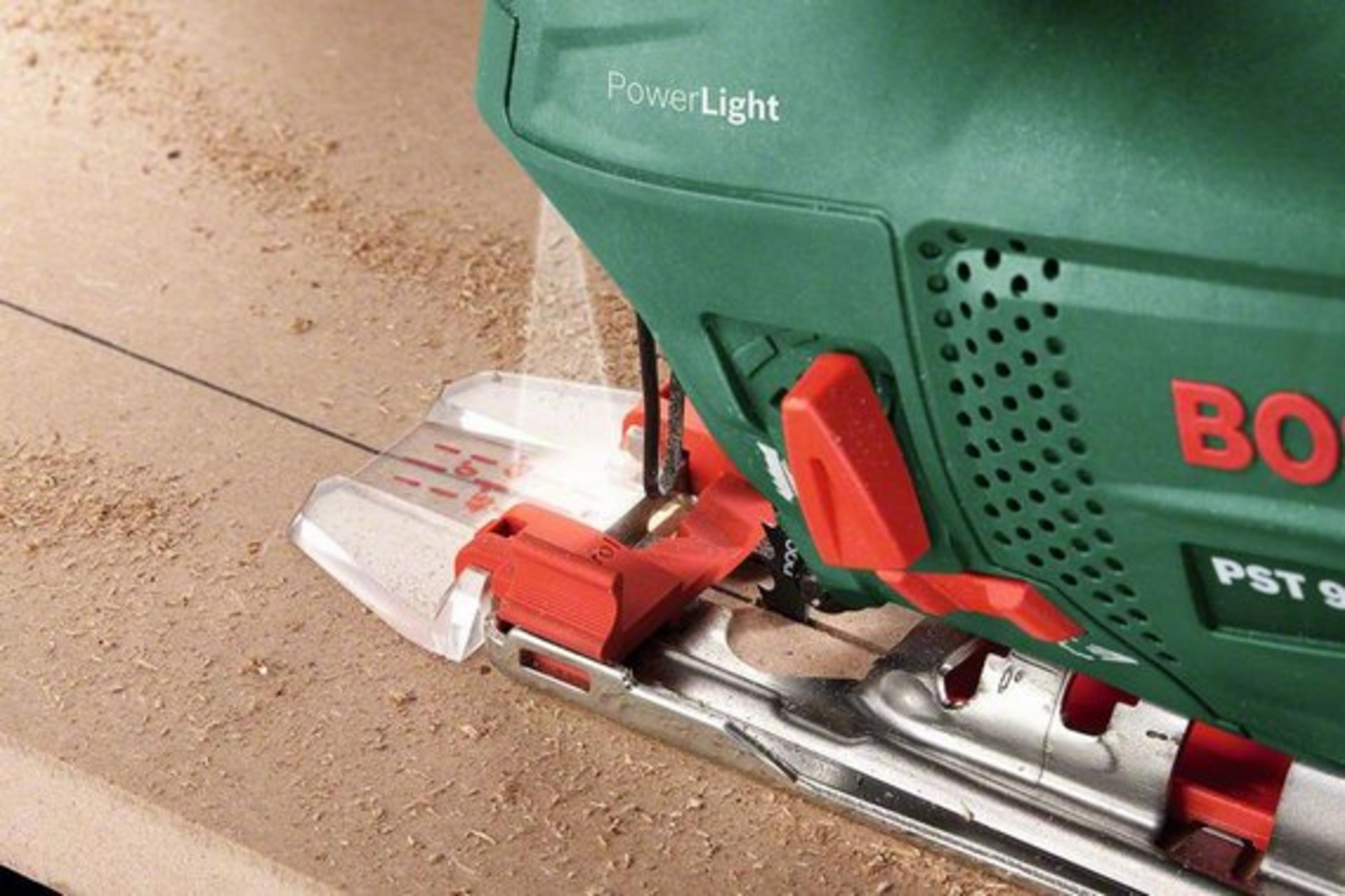 Zbliżenie zielonej wyrzynarki tnącej drewno z czerwonym przyciskiem i osłoną.