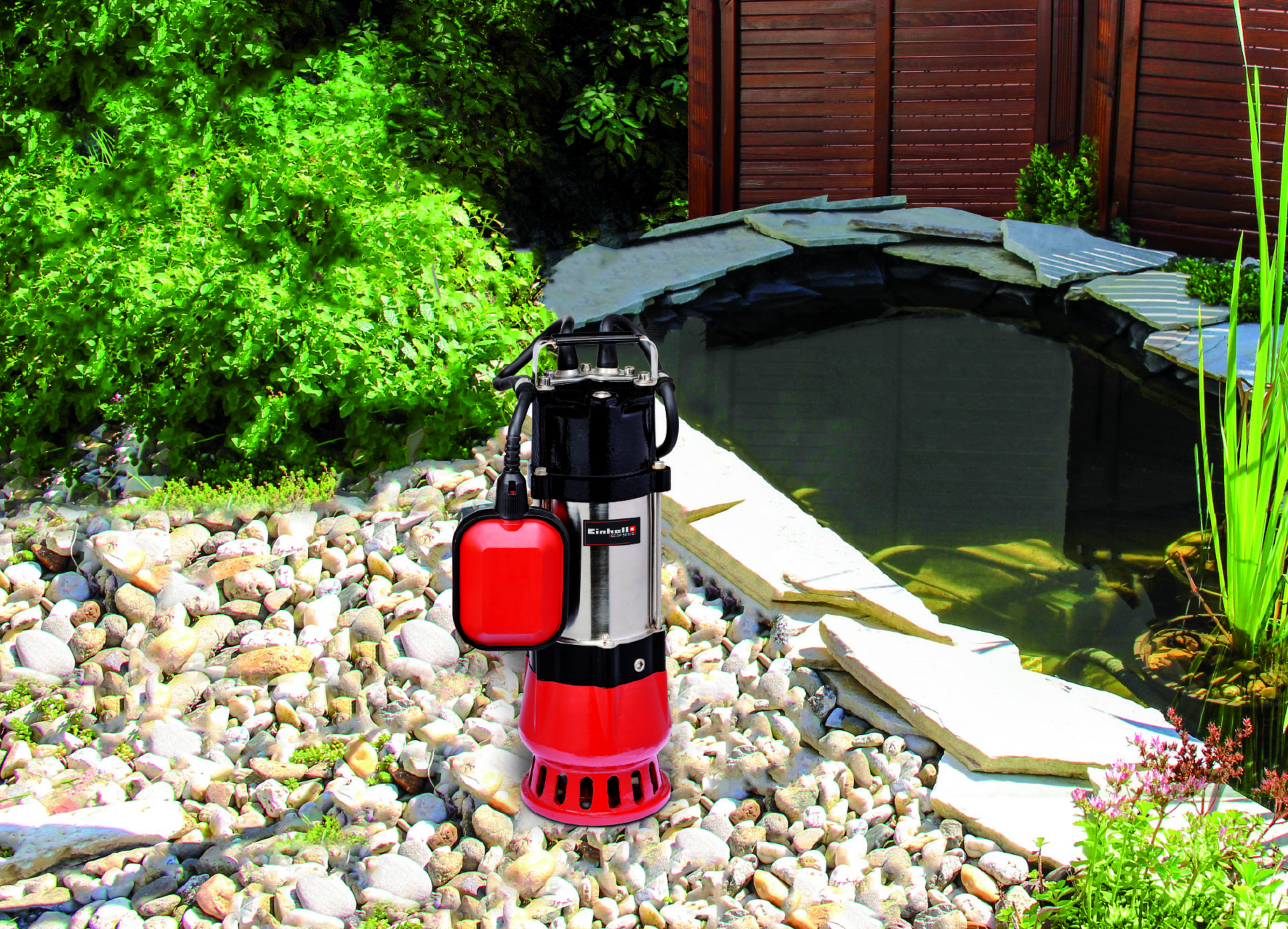 Czerwono-czarna pompa wodna stoi wśród skał w pobliżu stawu z zielonymi roślinami.