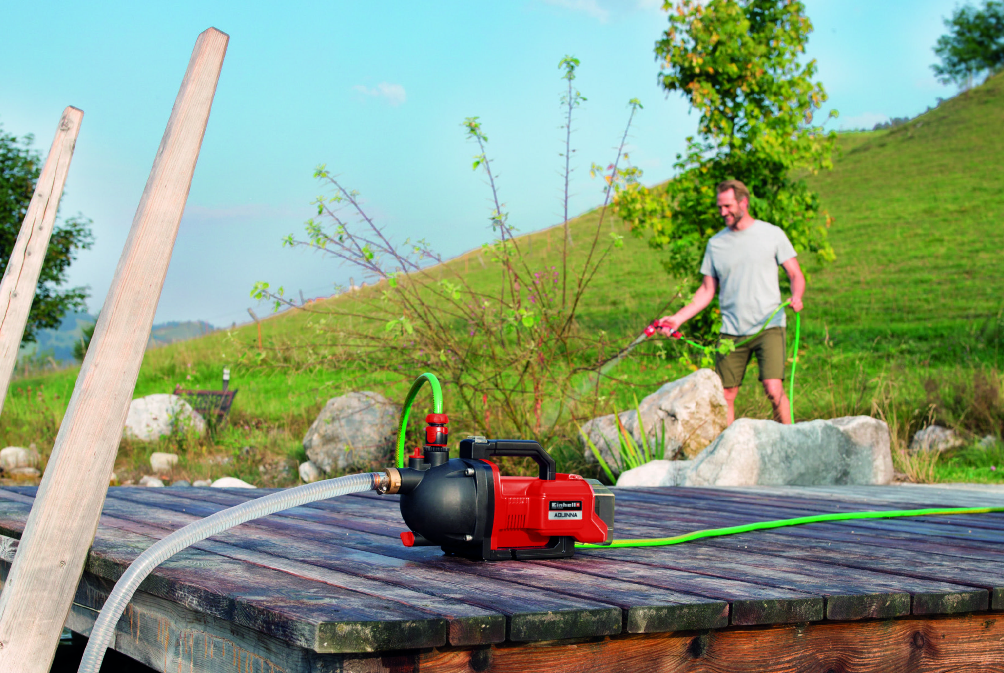 Mężczyzna używa węża do podlewania roślin. Czerwona i czarna pompa na drewnianym podeście.